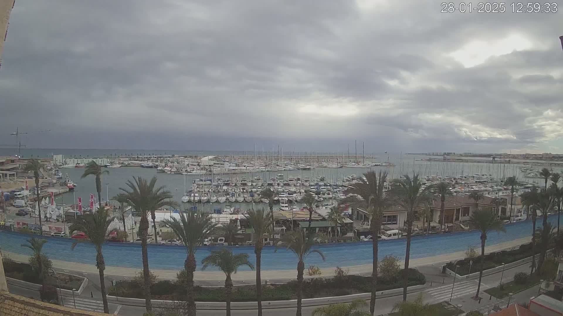 A crowded marina filled with sailboats and motorboats is viewed from above on an overcast day.