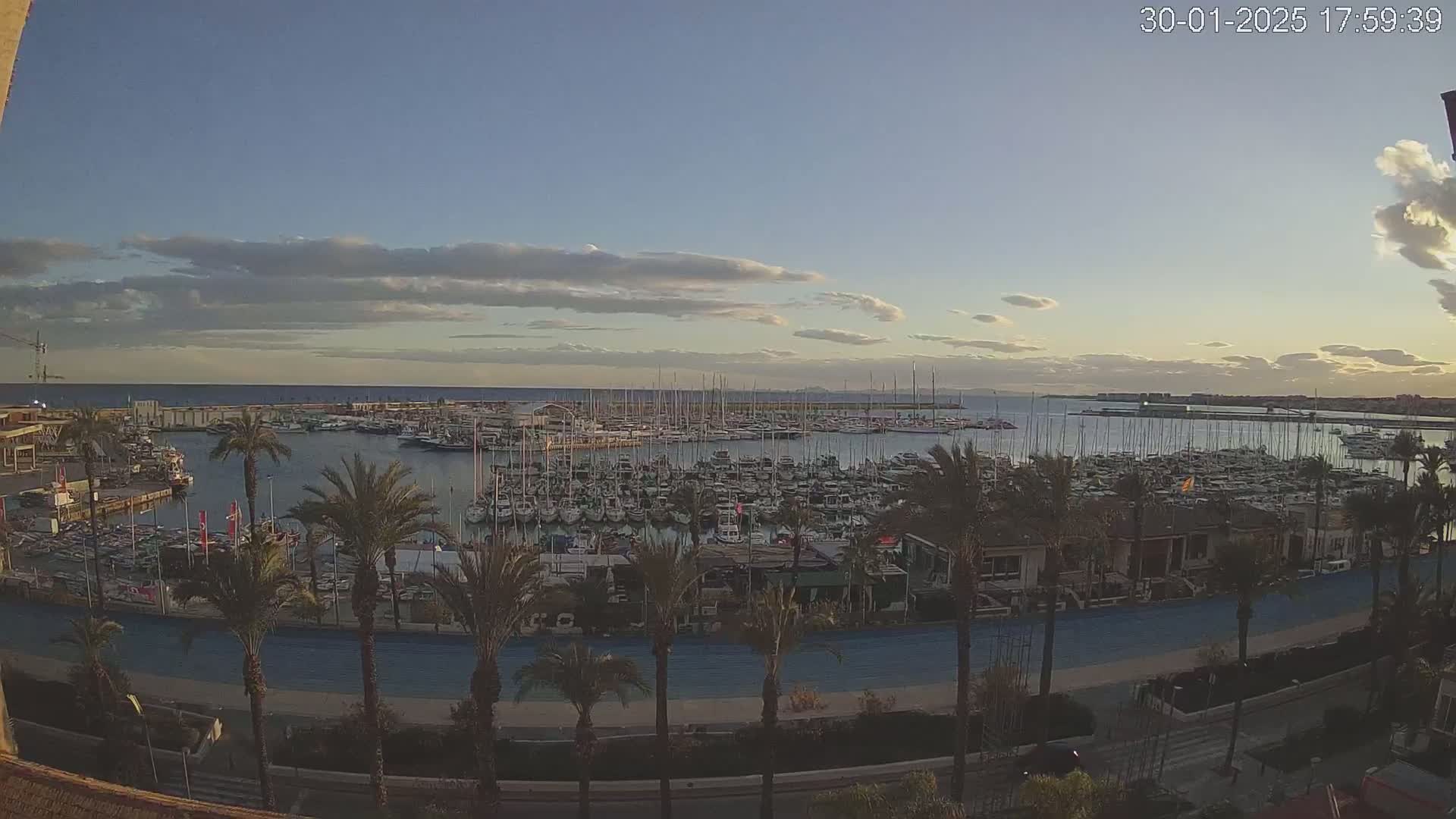 A marina filled with numerous sailboats and motorboats is visible under a partly cloudy sunset sky.