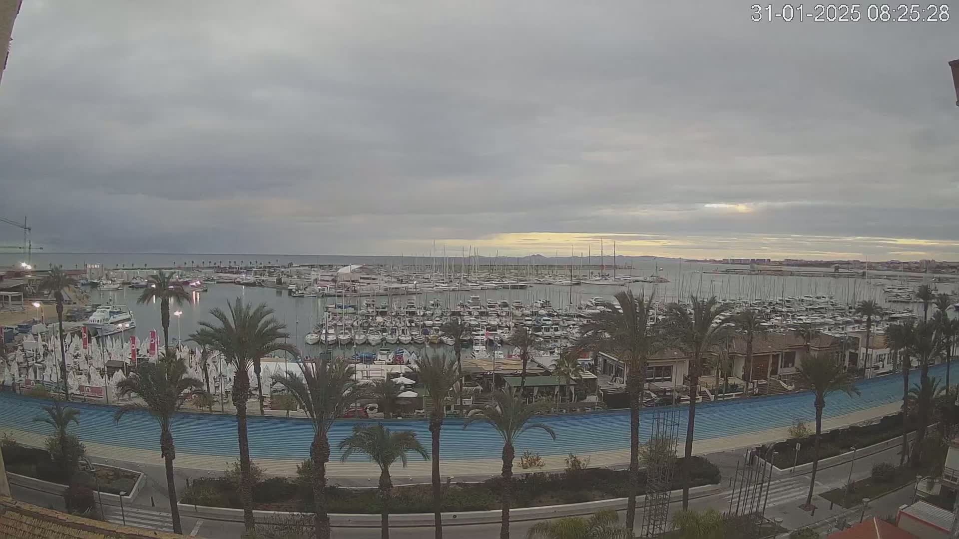 A large marina filled with numerous sailboats and motorboats is viewed from above under an overcast sky.