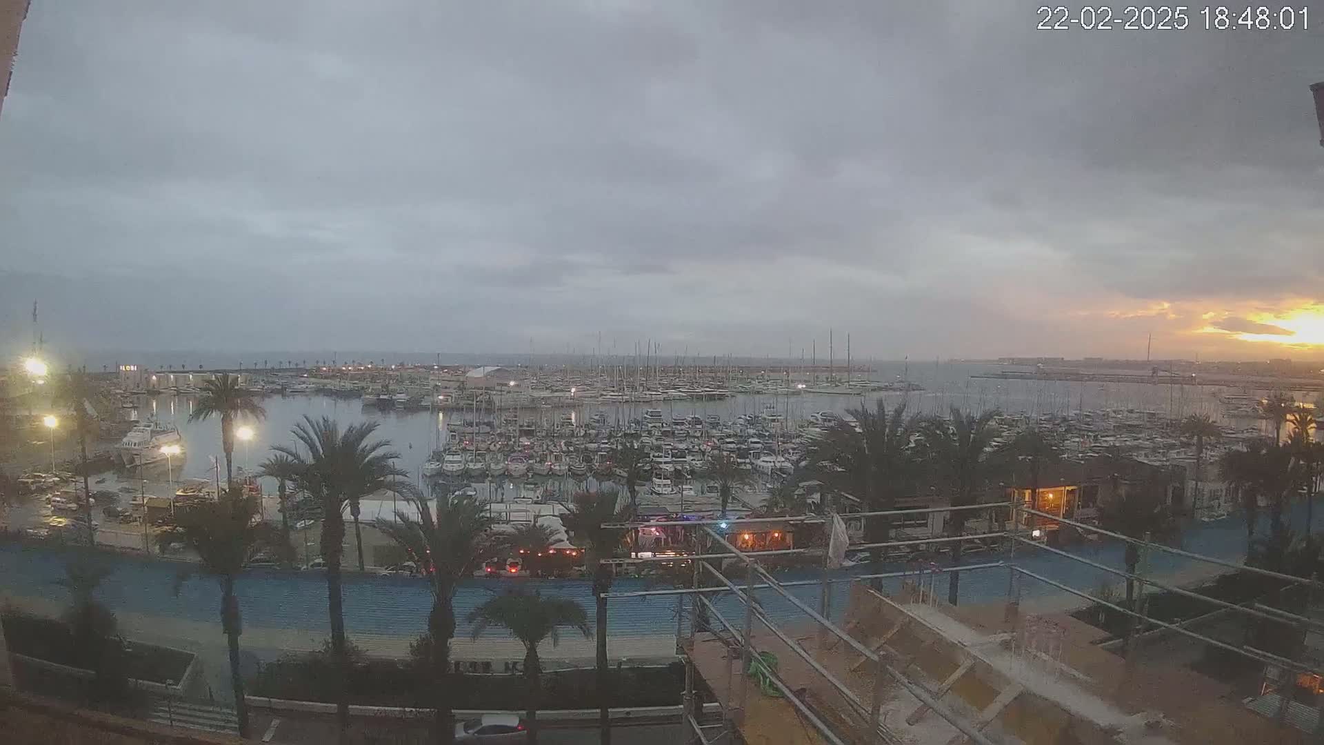 A large marina filled with boats is seen at sunset under an overcast sky.