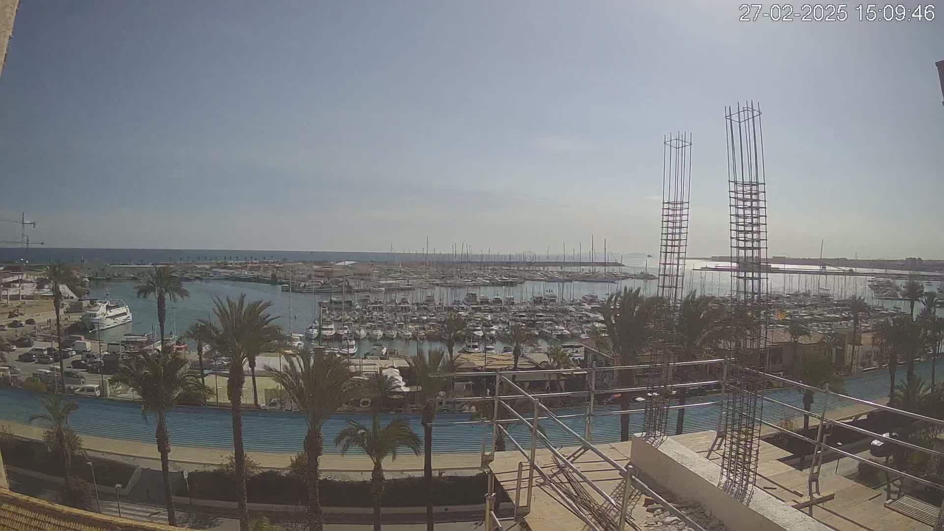 A sunny day overlooking a marina filled with numerous boats, palm trees lining a promenade, and construction underway in the foreground.