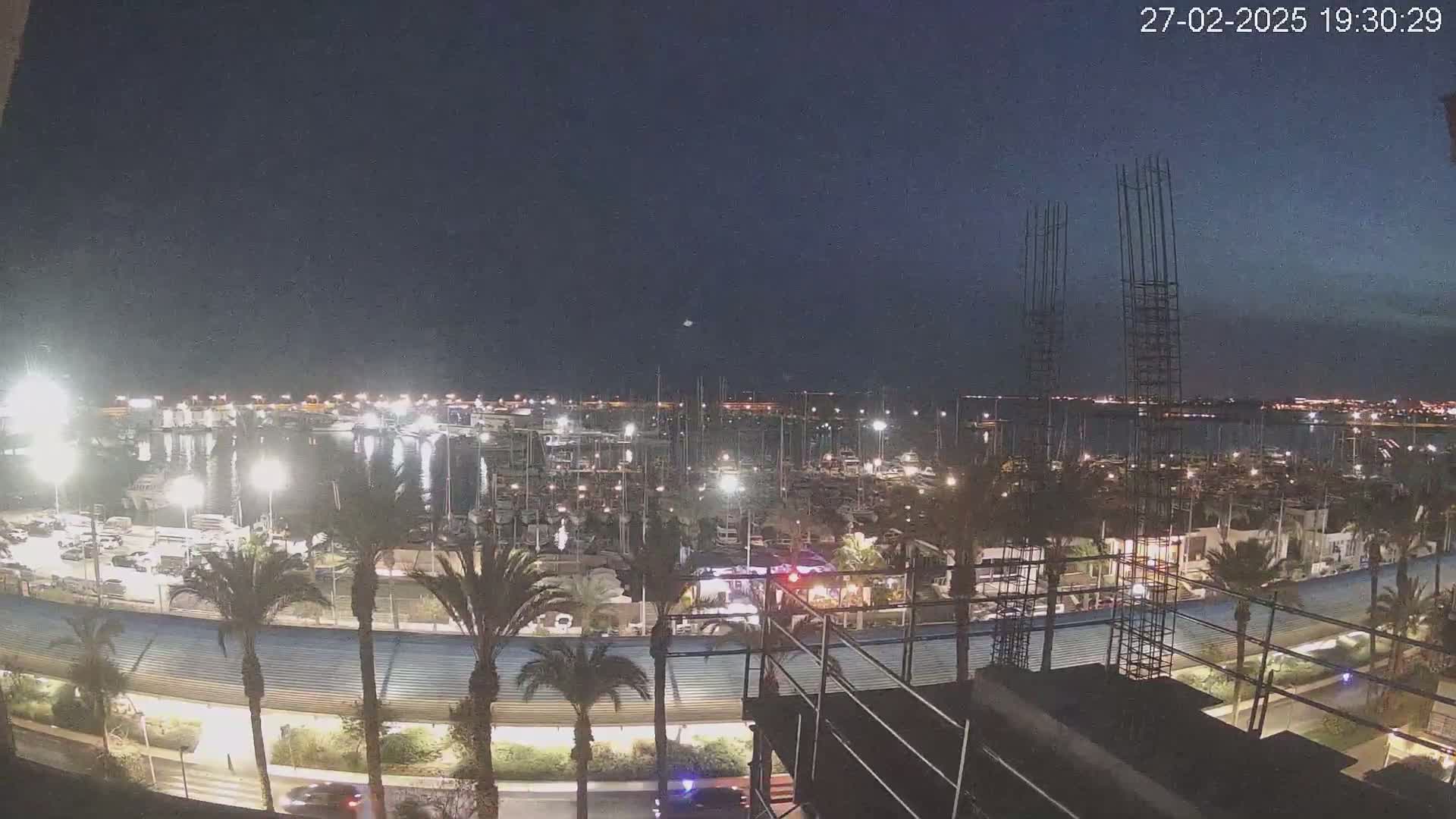 A nighttime view of a marina filled with boats, illuminated by lights, under a clear, dark sky.
