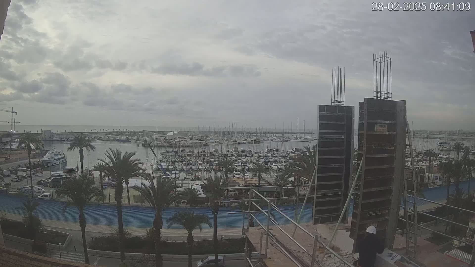 A cloudy day overlooks a harbor filled with numerous boats and yachts, with construction underway on a building in the foreground.