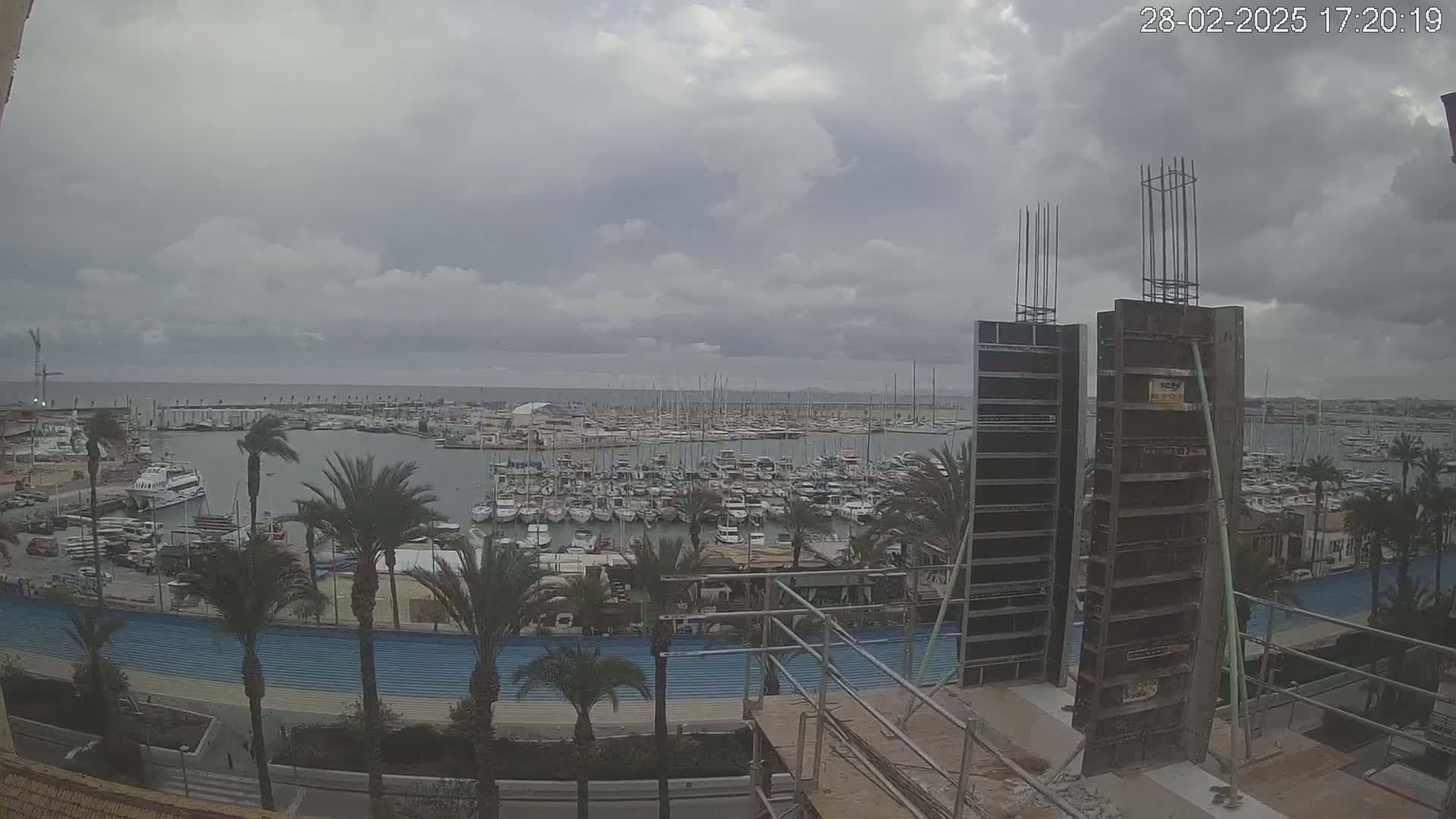 A marina filled with numerous boats is viewed from a partially constructed building under an overcast sky.