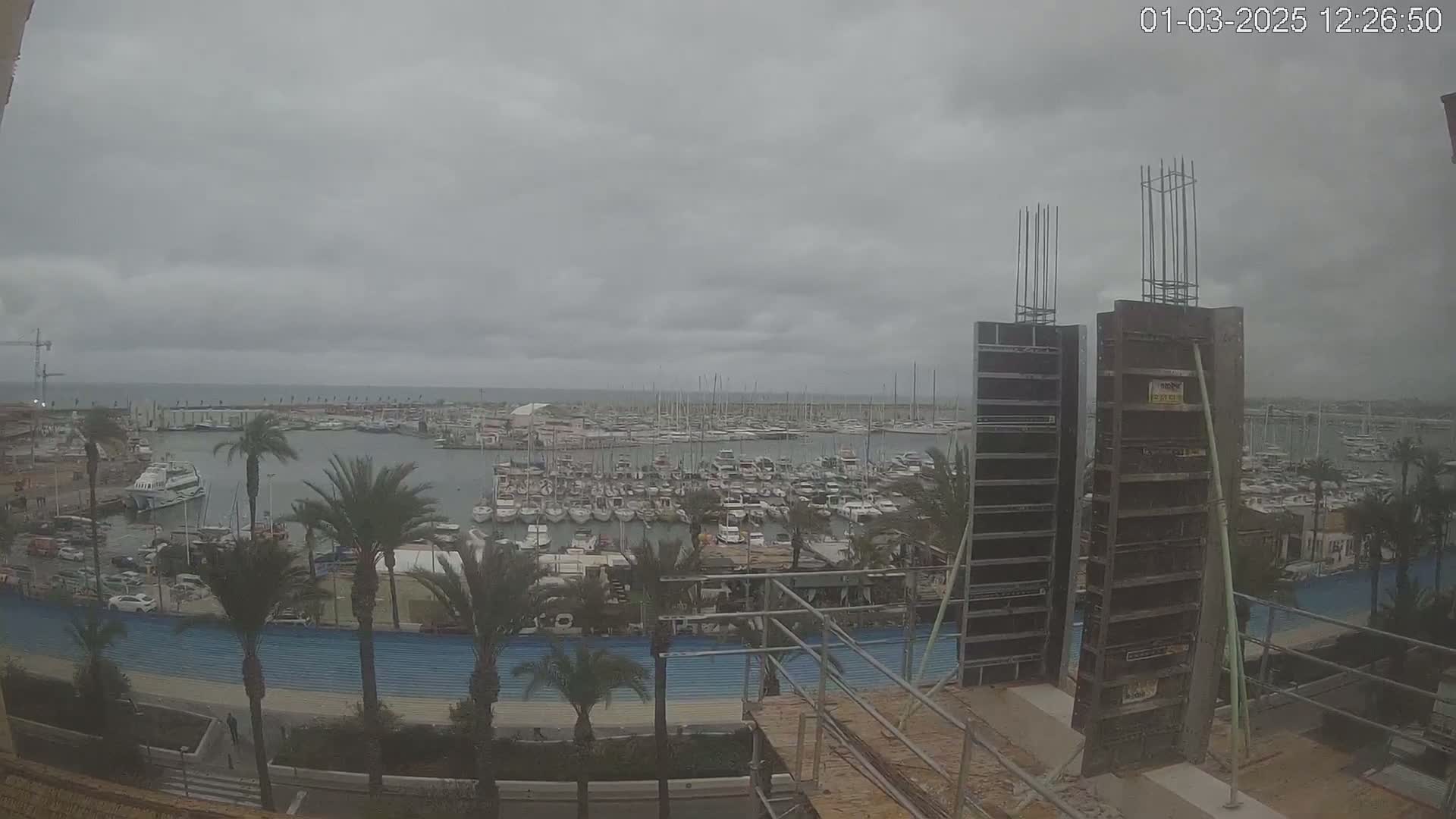 A harbor filled with numerous boats is viewed from a construction site on an overcast day.