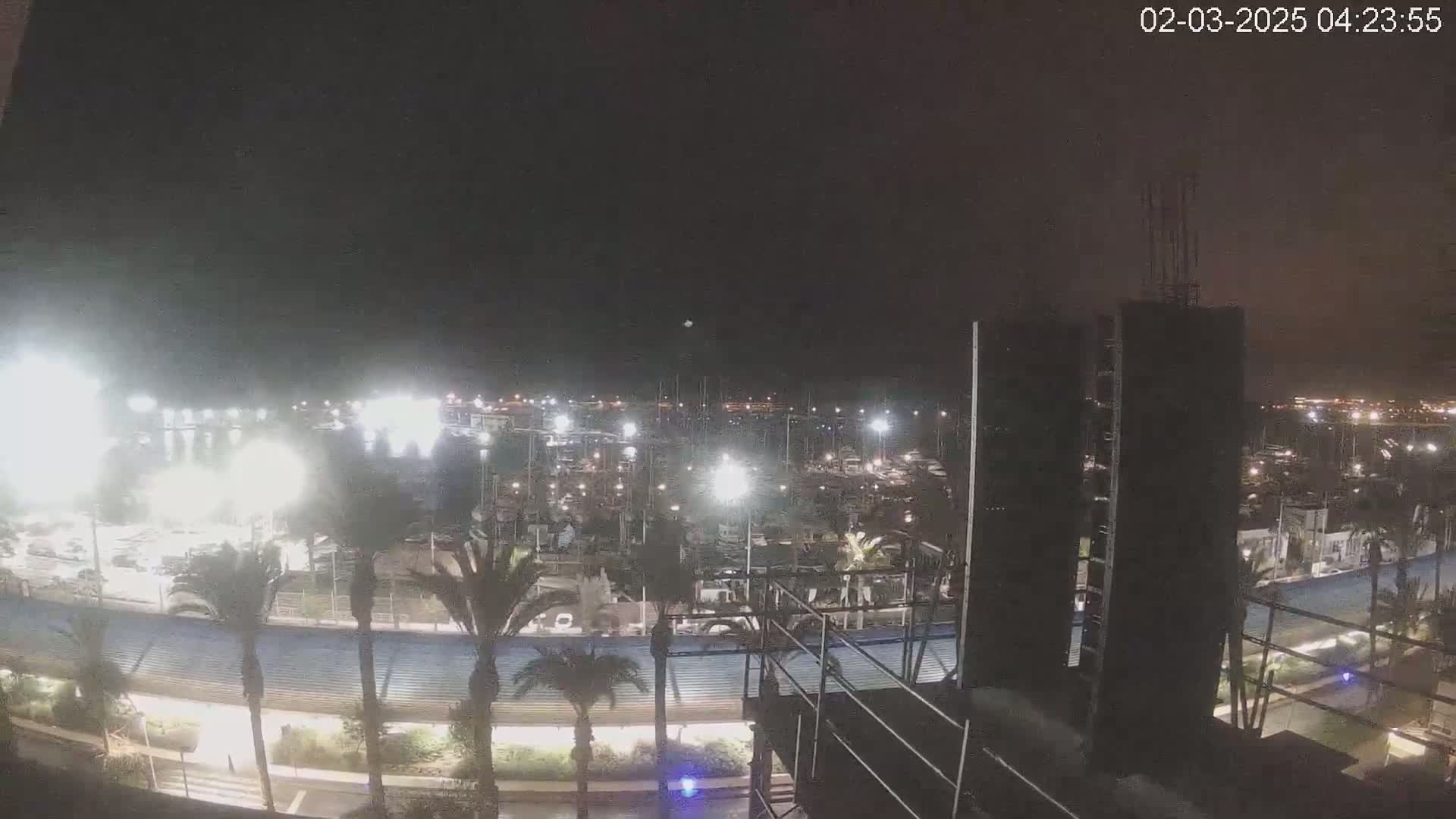 A nighttime view of a marina filled with boats, illuminated by bright lights, under a dark, clear sky.