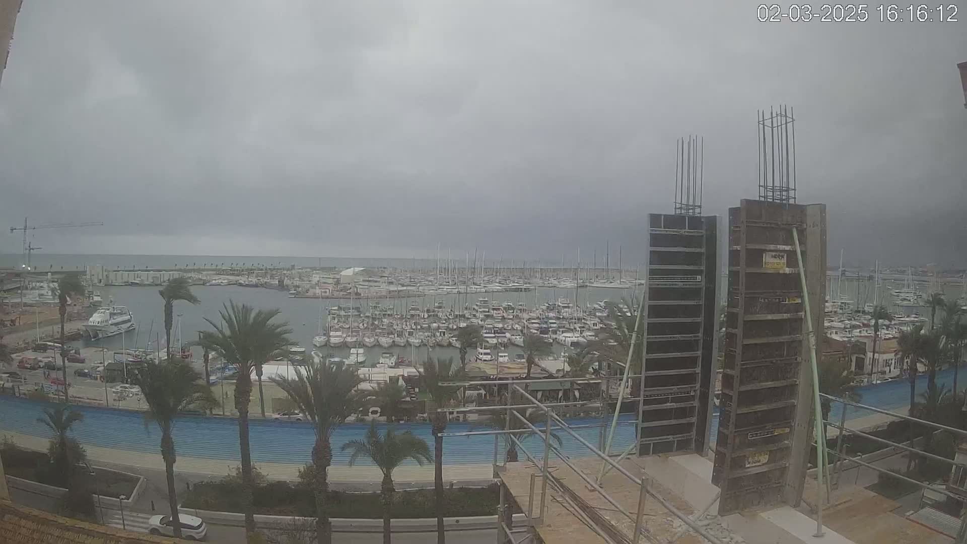 A harbor filled with many boats is seen from an elevated vantage point under an overcast sky, with construction underway in the foreground.