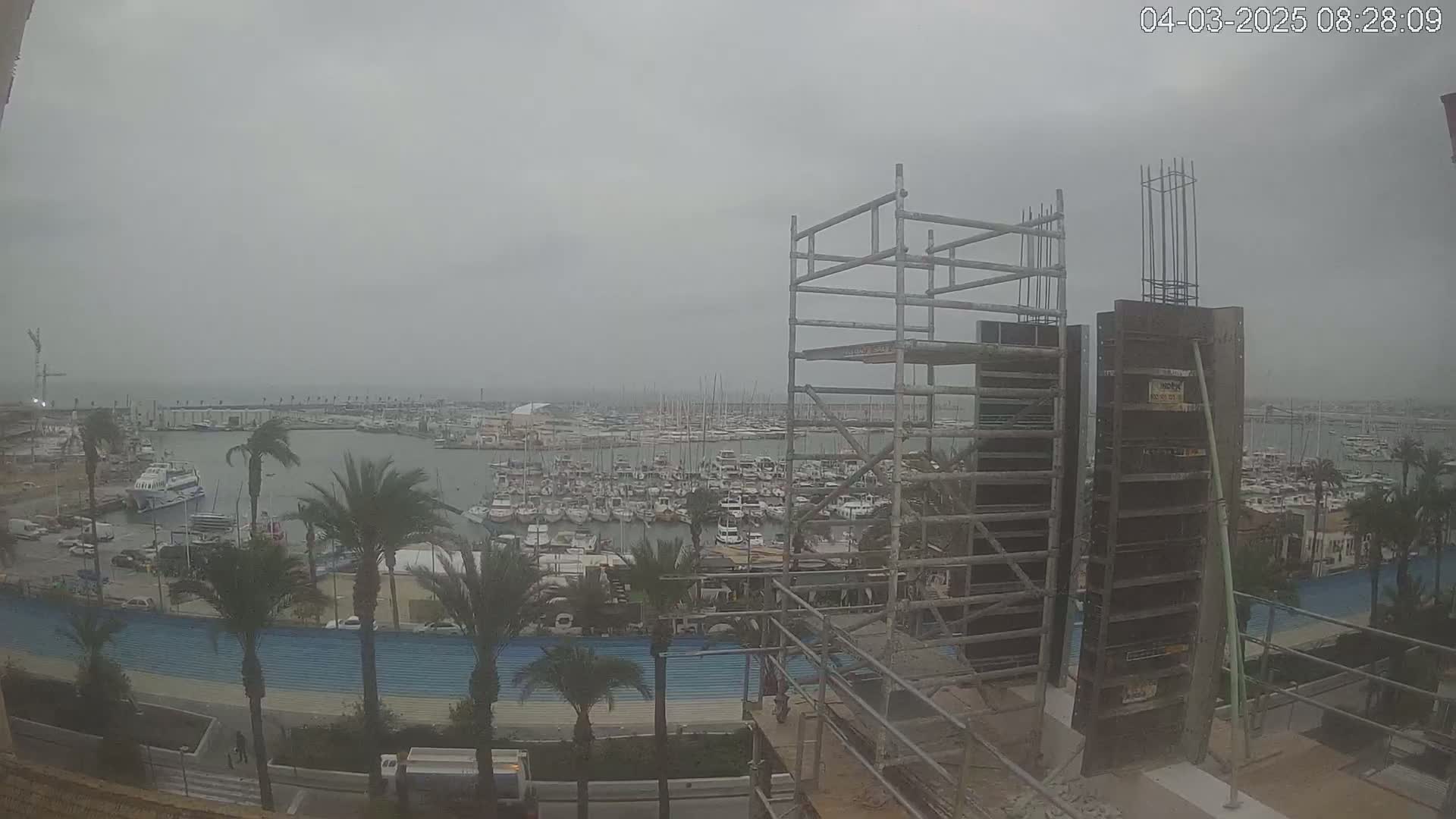 A construction site with scaffolding and formwork overlooks a marina filled with numerous boats on an overcast day.