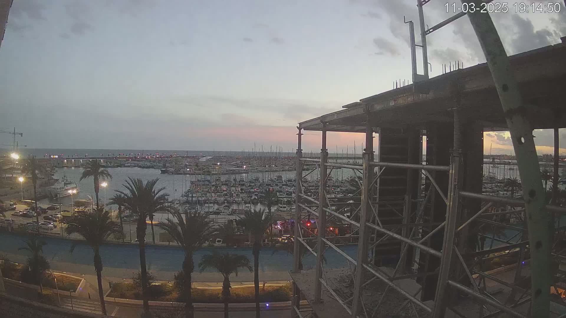 A marina filled with boats is visible at dusk from a construction site framed by scaffolding.