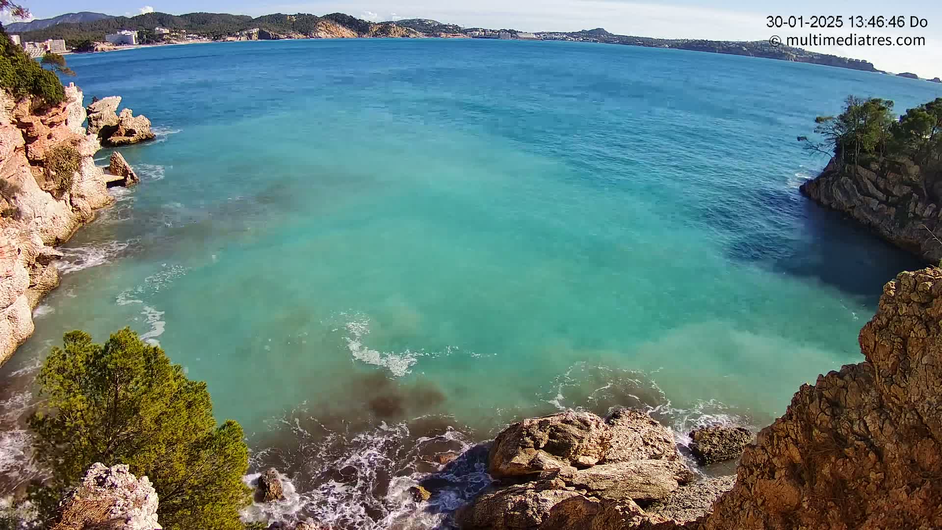 A cove of clear, turquoise water is nestled between rocky, tan cliffs on a sunny day.