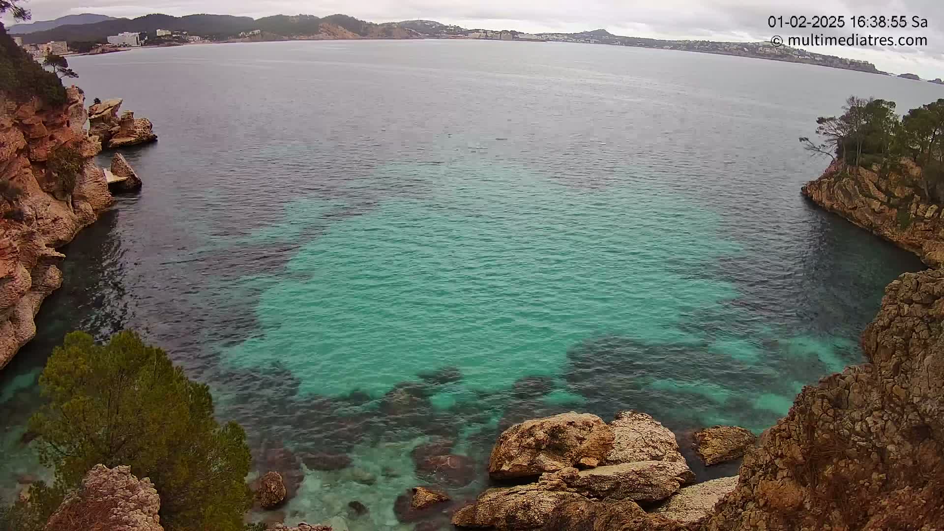 A cove of teal water is nestled between rocky, tan cliffs under an overcast sky.