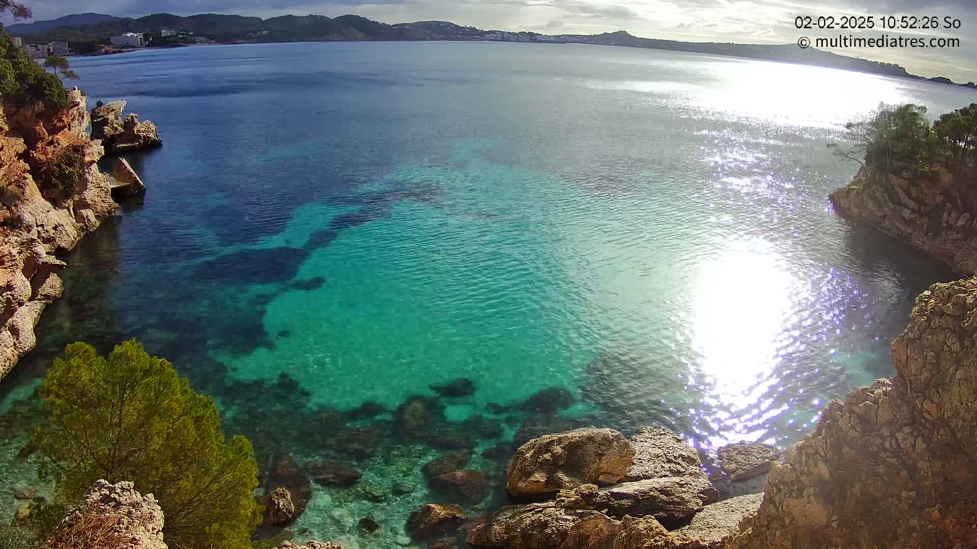 Clear, turquoise water fills a cove surrounded by rocky, tan cliffs under a mostly sunny sky.