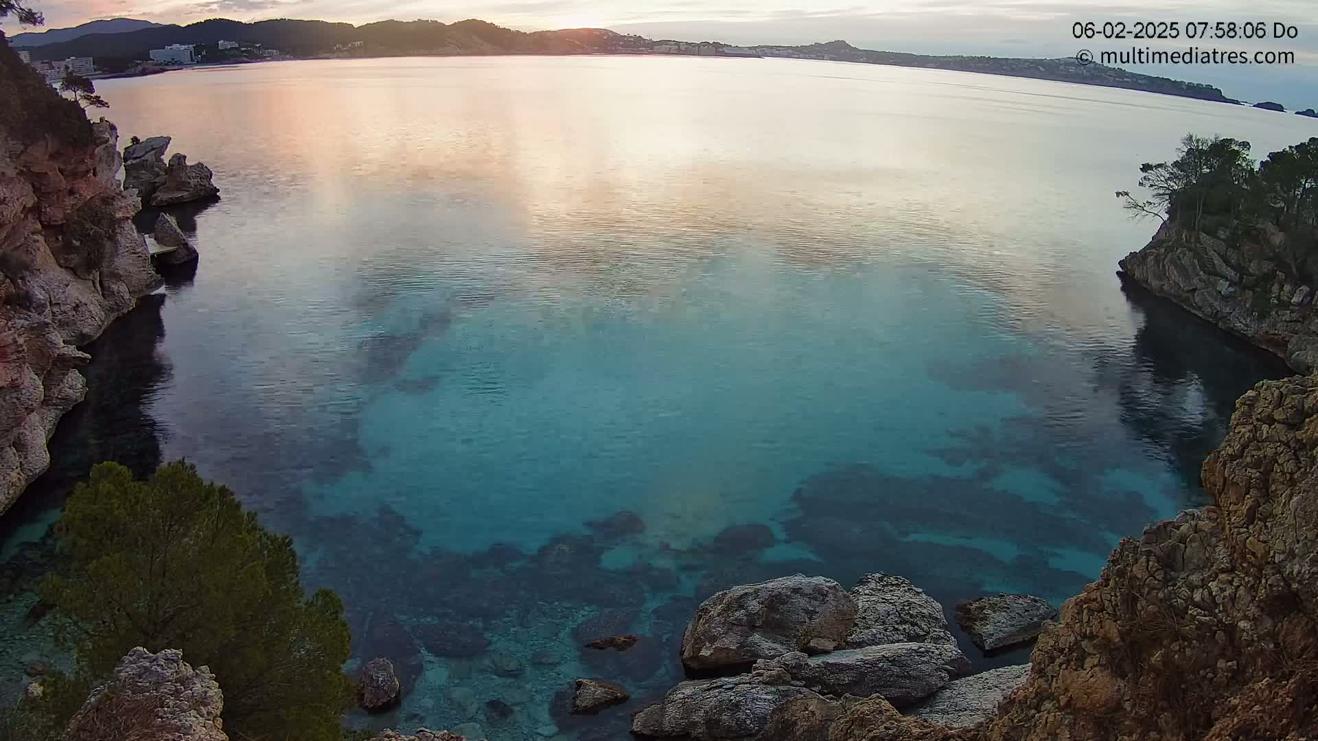 Calm, clear turquoise water in a secluded cove surrounded by rocky cliffs under a partly cloudy sunrise sky.