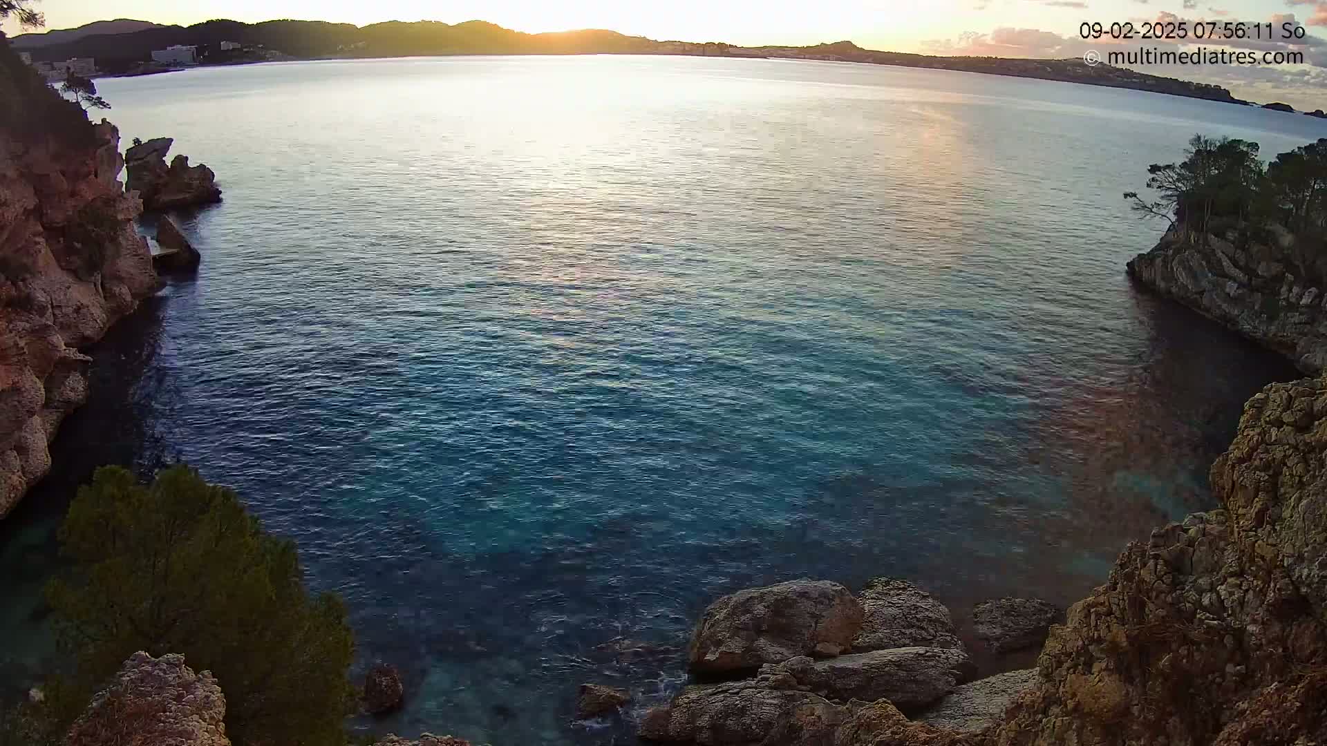 Calm, blue water in a cove bordered by rocky cliffs at sunrise.