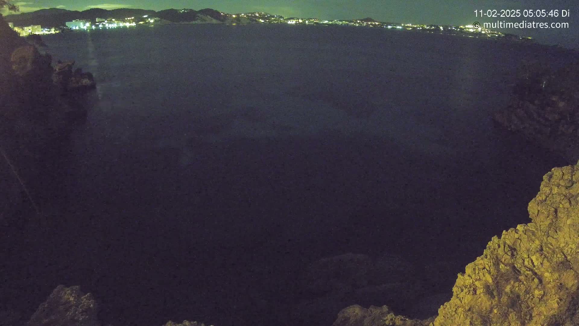 A nighttime view of a dark body of water with a distant, faintly lit cityscape under a clear sky.