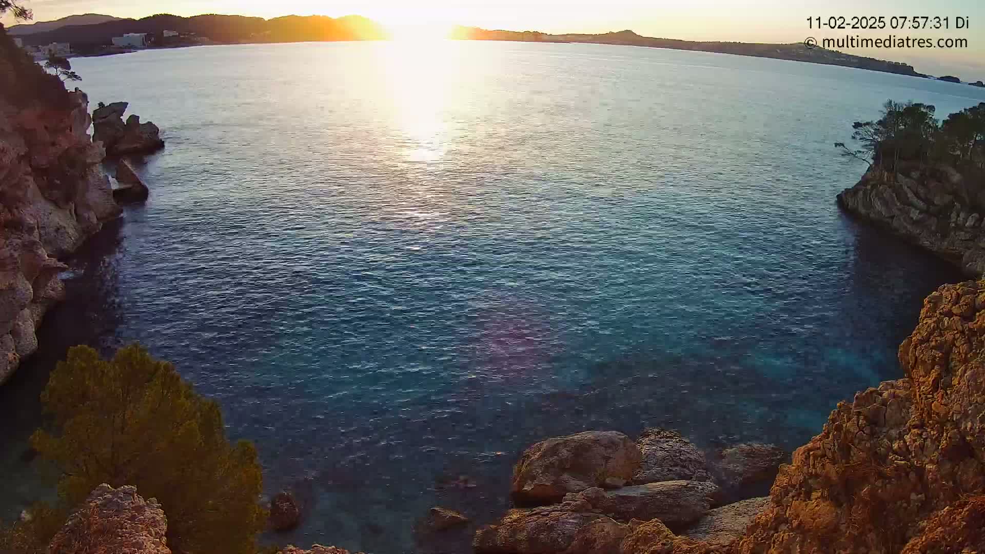 A calm, dark-blue sea is nestled between rocky, orange-hued cliffs at sunset.