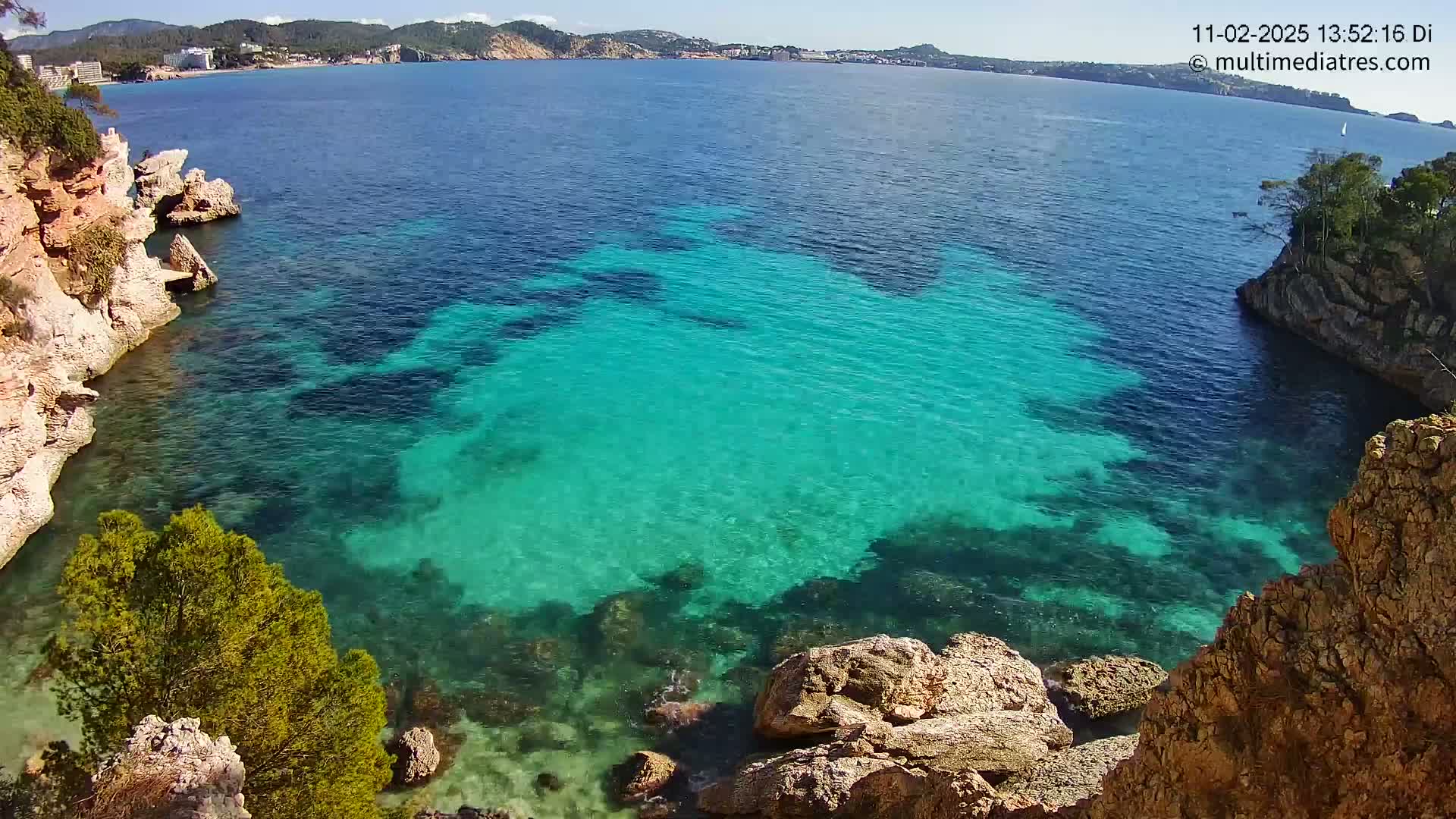 A cove of bright turquoise water is nestled between rocky cliffs on a sunny day.