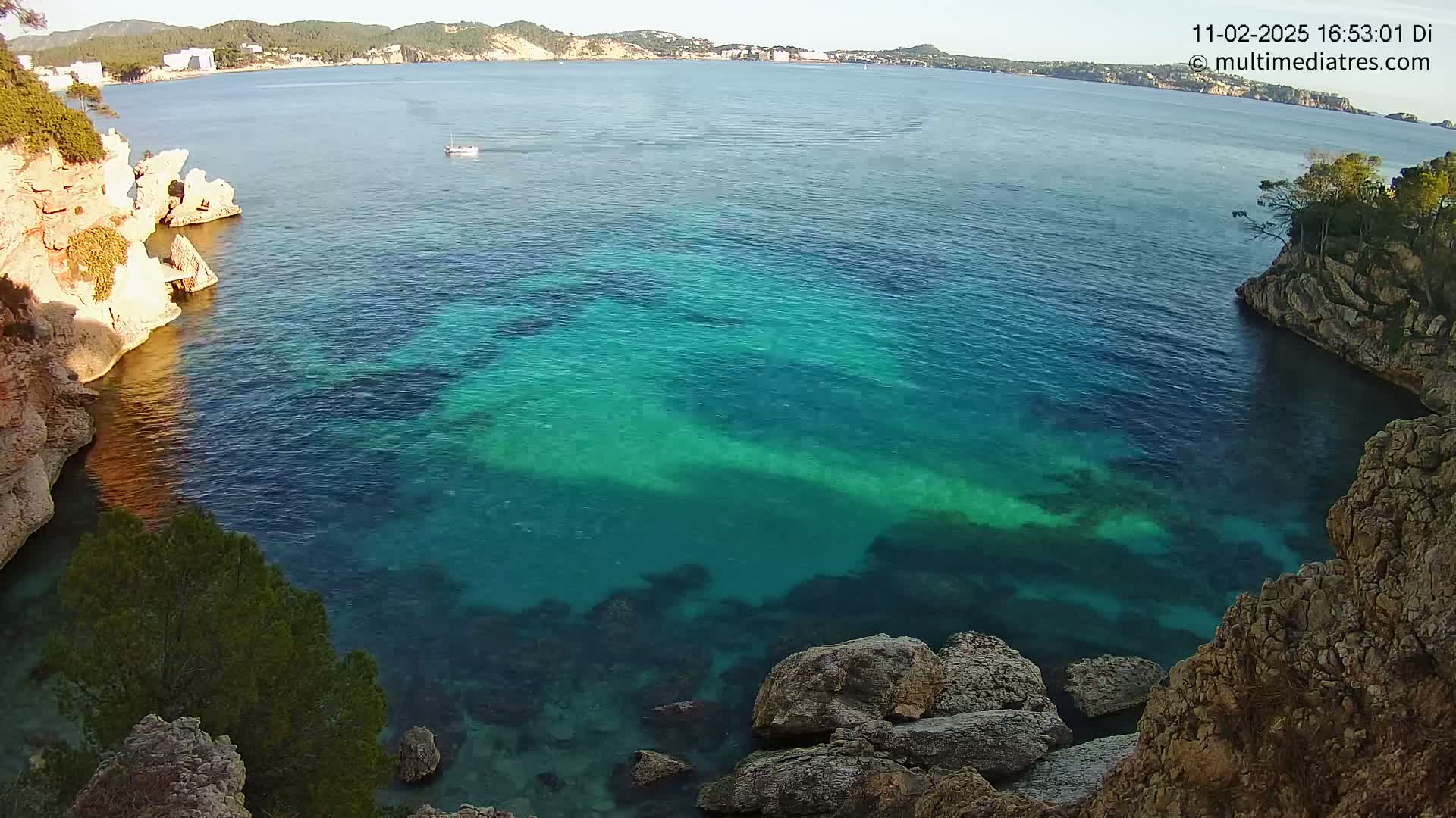 A tranquil cove with clear, turquoise water is nestled between rocky cliffs, under a sunny sky.