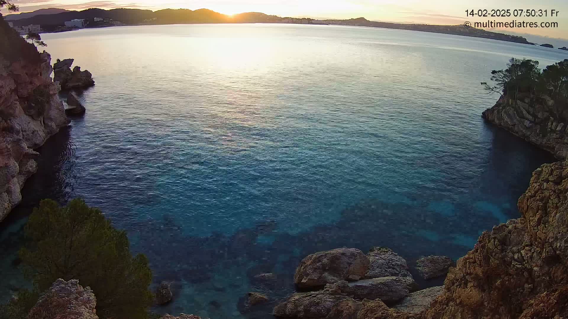 A calm, blue-green sea is nestled between rocky cliffs at sunrise.