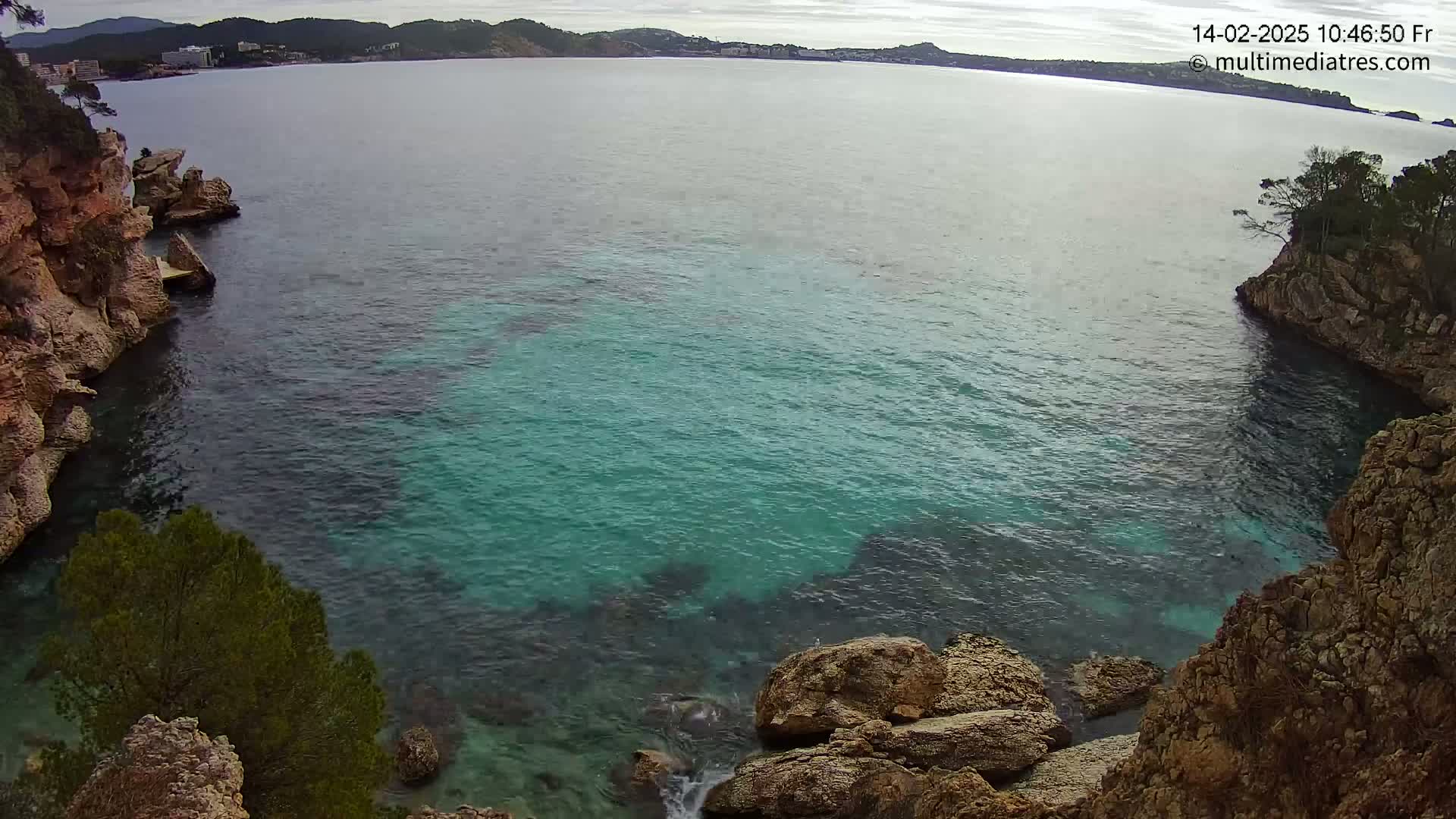 A cove of clear, teal water is nestled between rocky, tan cliffs on a cloudy day.