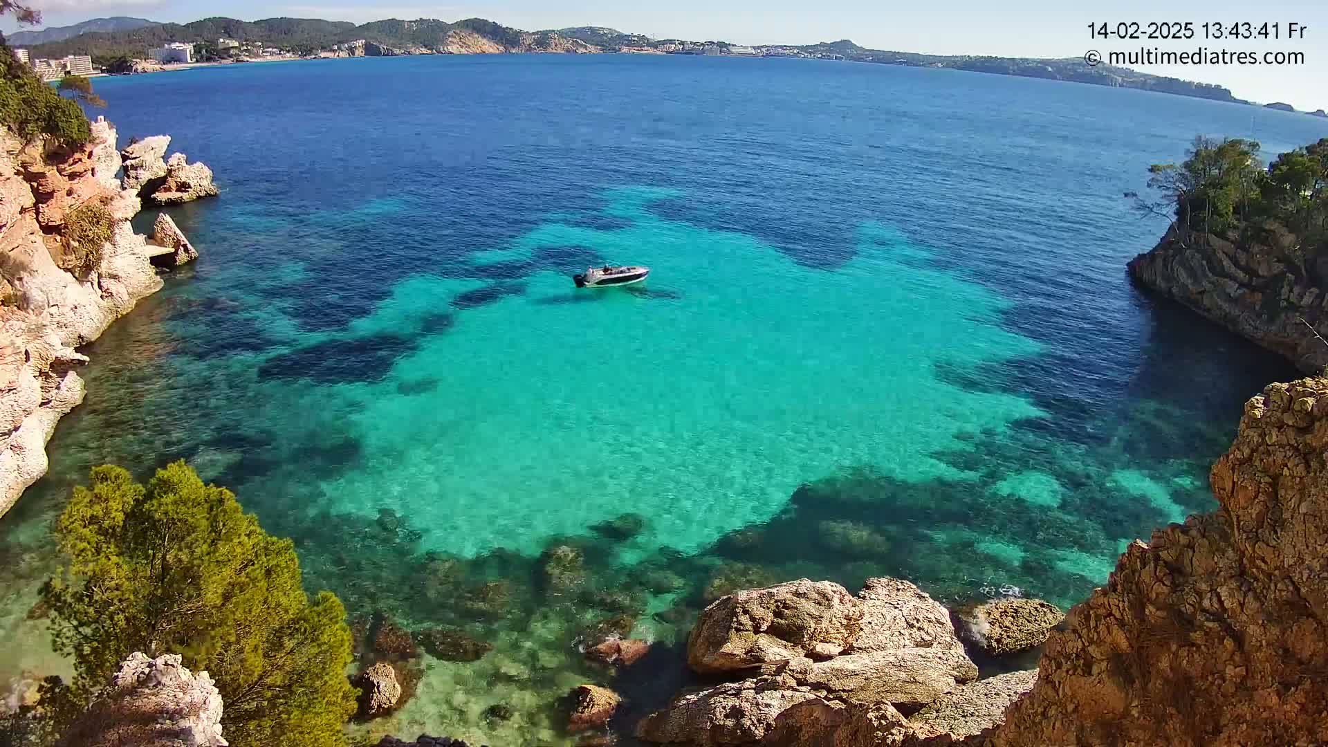 A small boat rests in a calm, clear turquoise cove surrounded by rocky cliffs and vegetation, under a sunny sky.