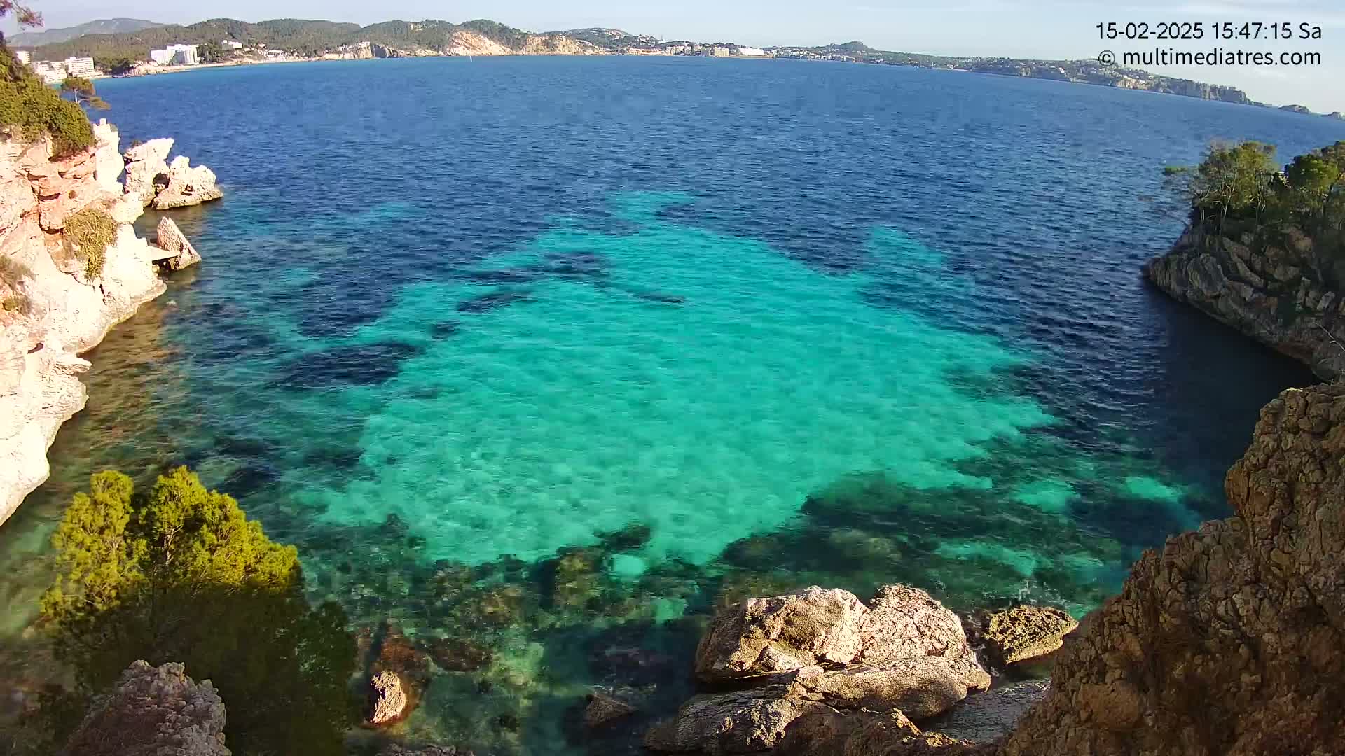 Brightly lit turquoise water fills a cove nestled between rocky, light-brown cliffs on a sunny day.