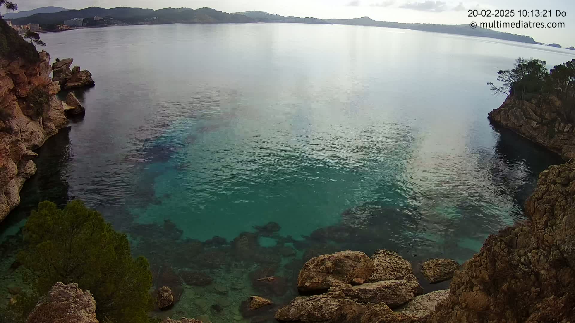 Clear, teal water fills a cove between rocky, tan cliffs under an overcast sky.