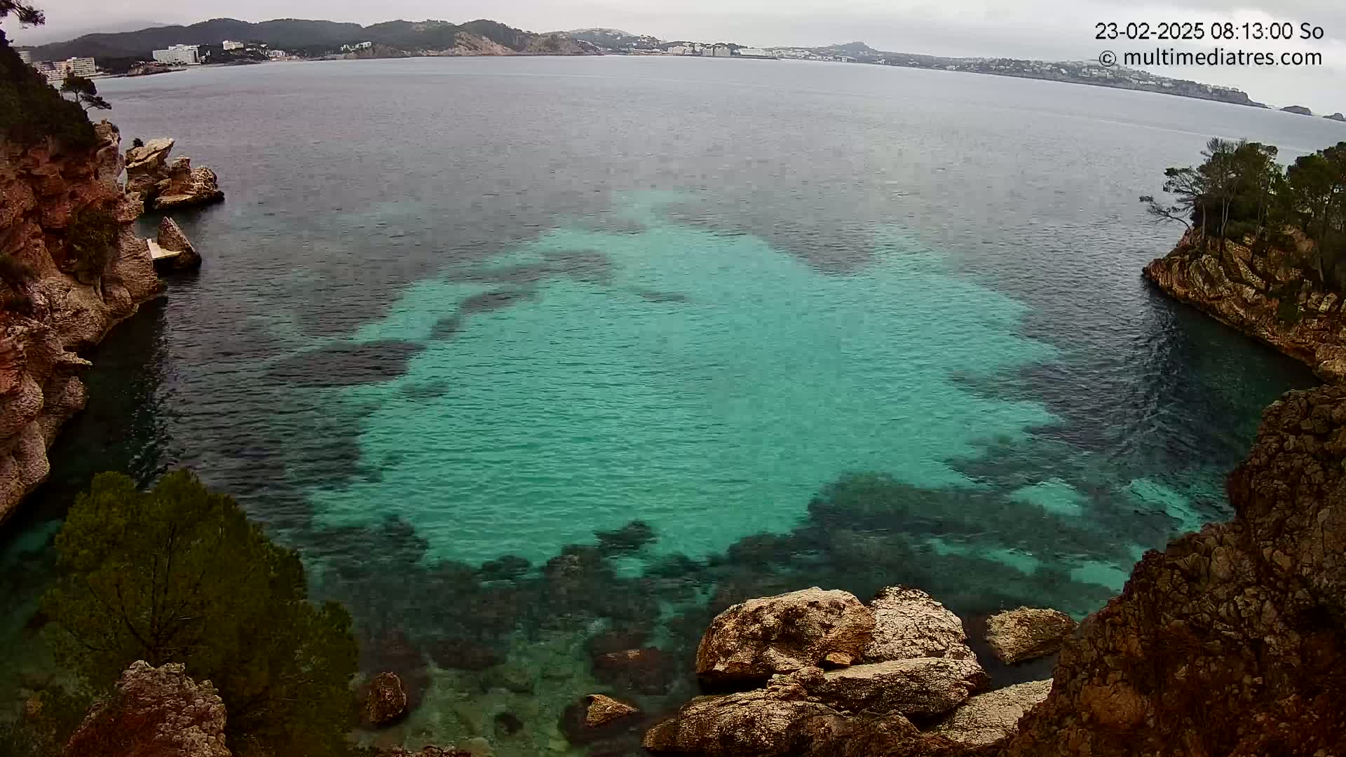 A cove of teal water surrounded by rocky, vegetated cliffs on an overcast day.