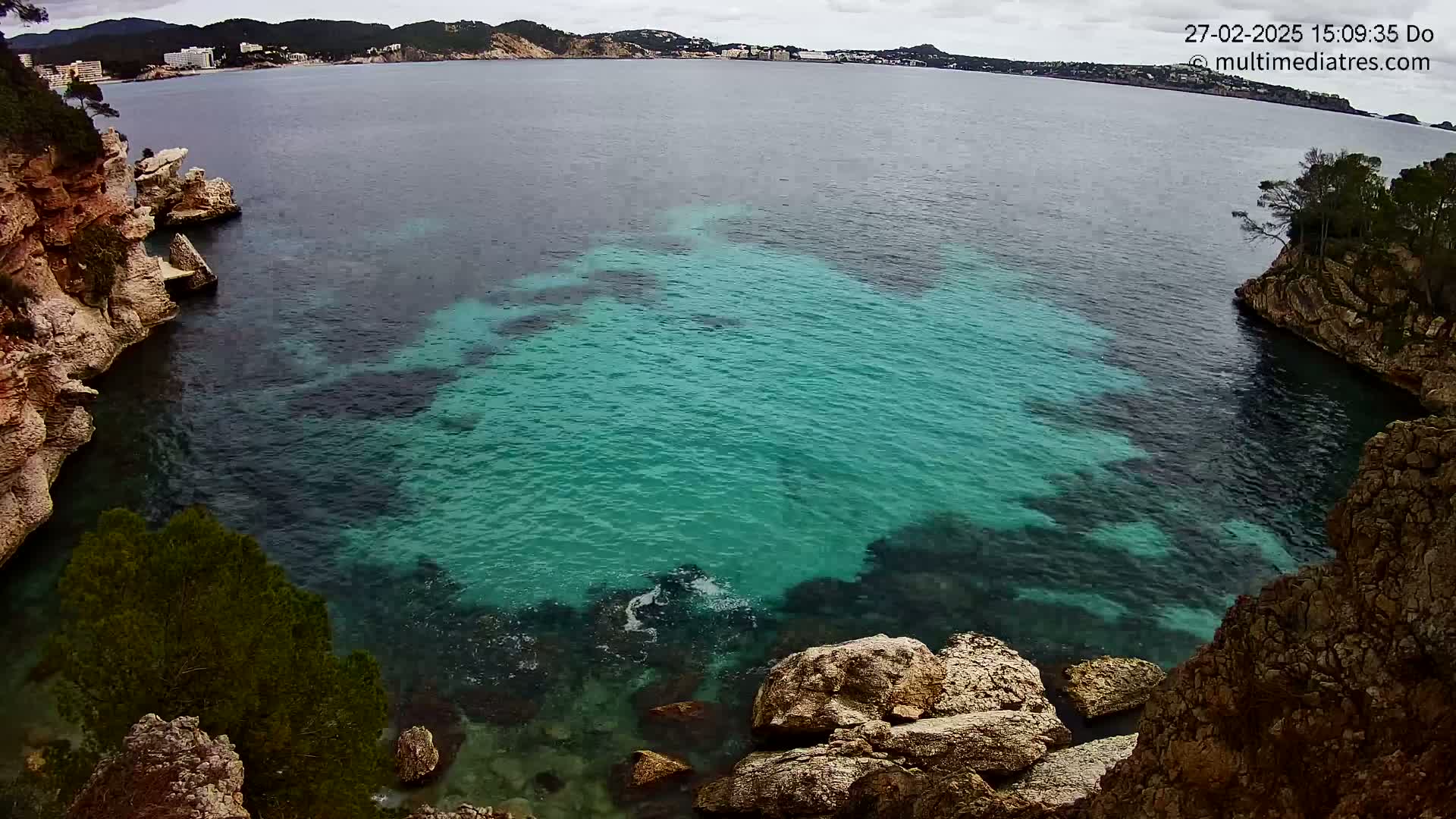 Bright teal water fills a cove between rocky, vegetated cliffs on an overcast day.