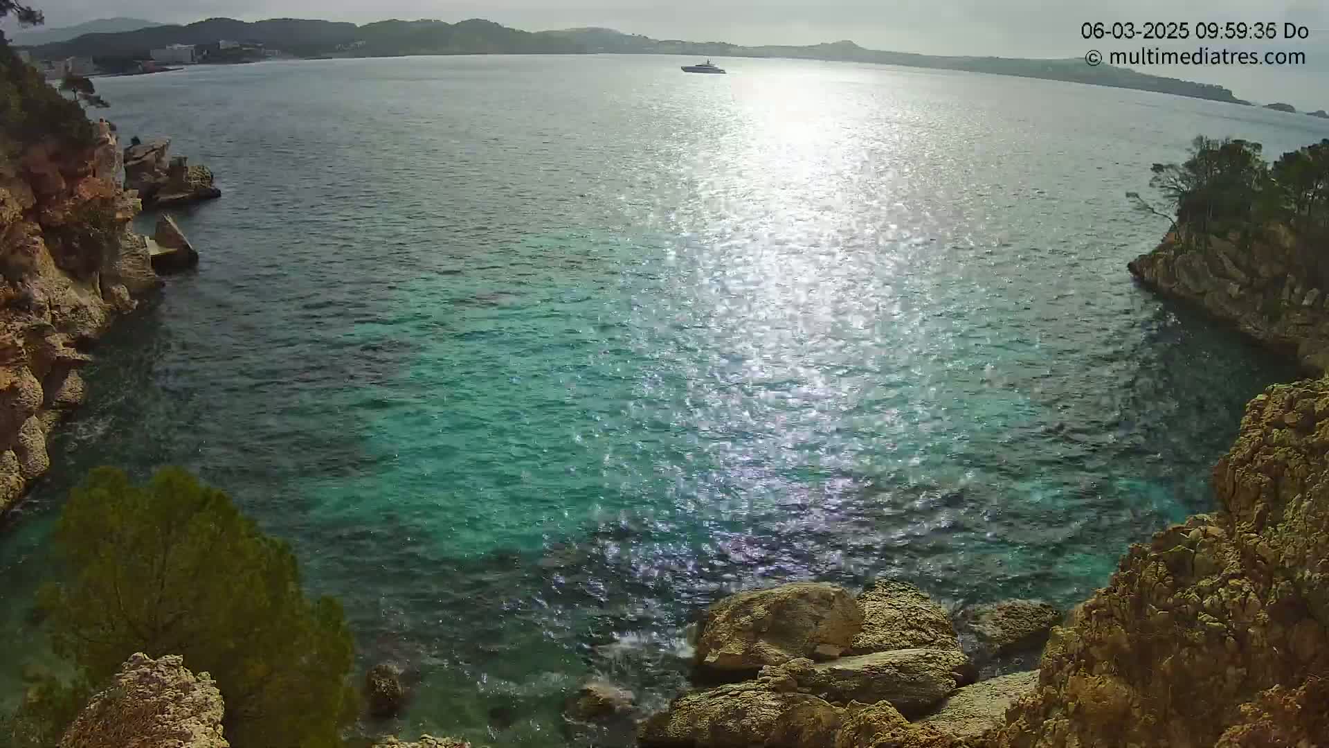 A sunny day reveals a tranquil cove of teal water nestled between rocky, cliffside shores, with a lone boat visible in the distance.