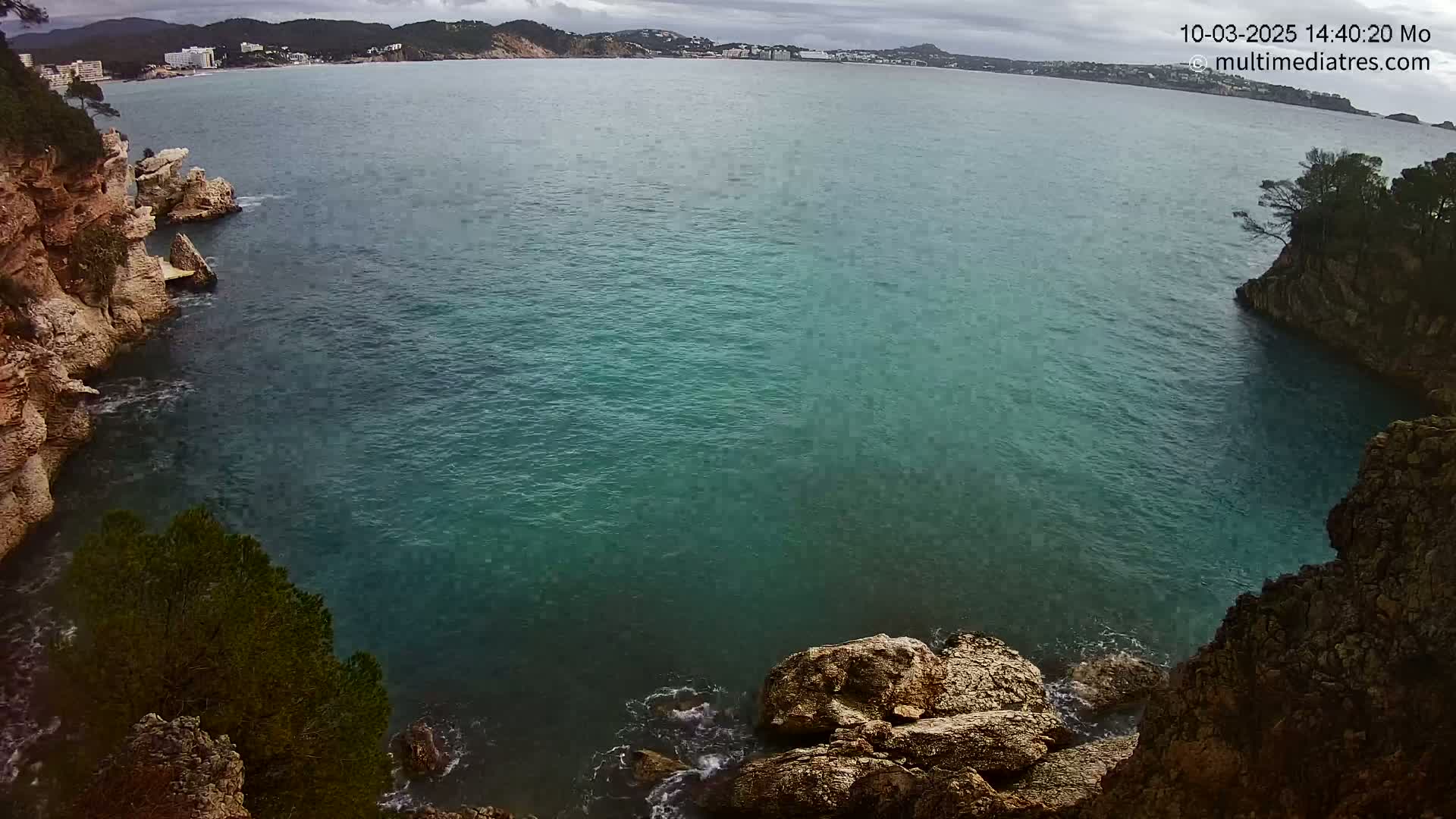 A teal-colored ocean is seen from a high vantage point between two rocky cliffs on an overcast day.