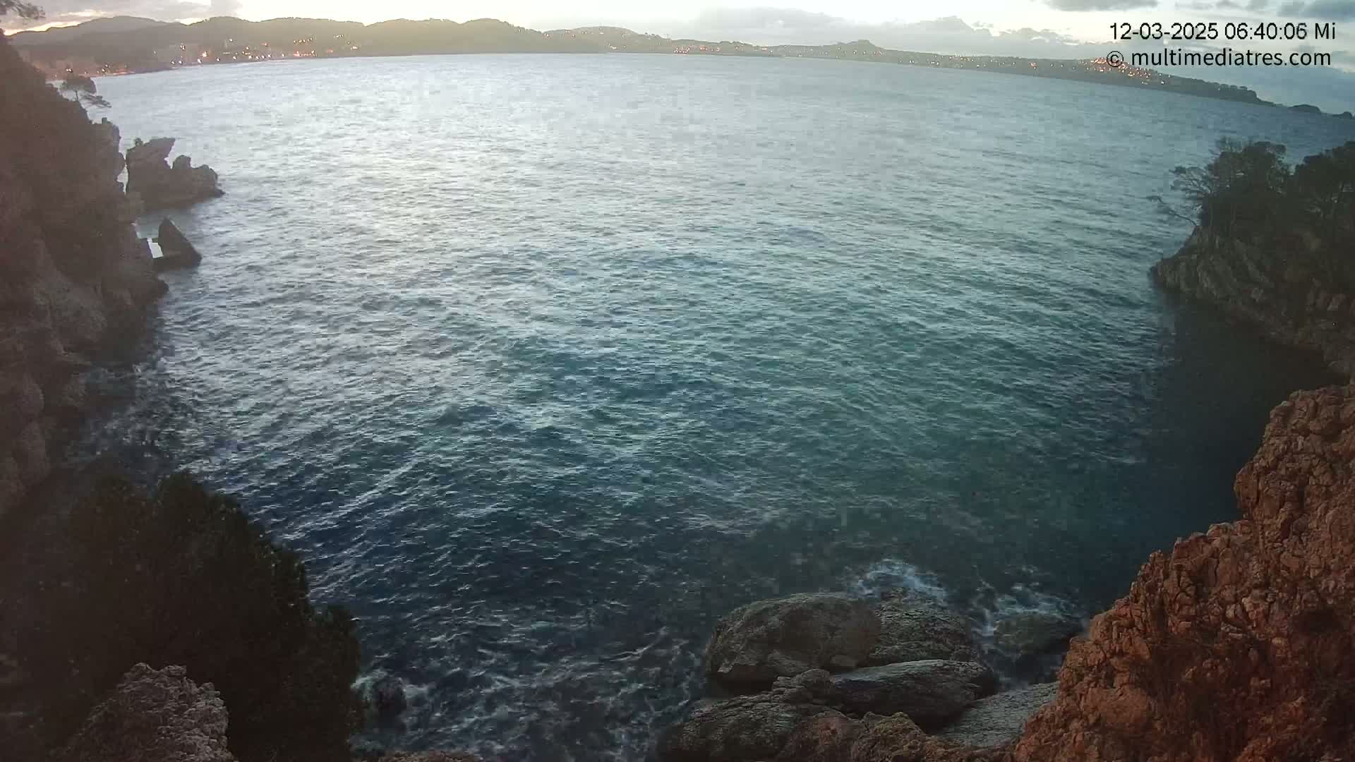 Rocky cliffs enclose a dark-blue sea under a mostly clear, dusky sky.