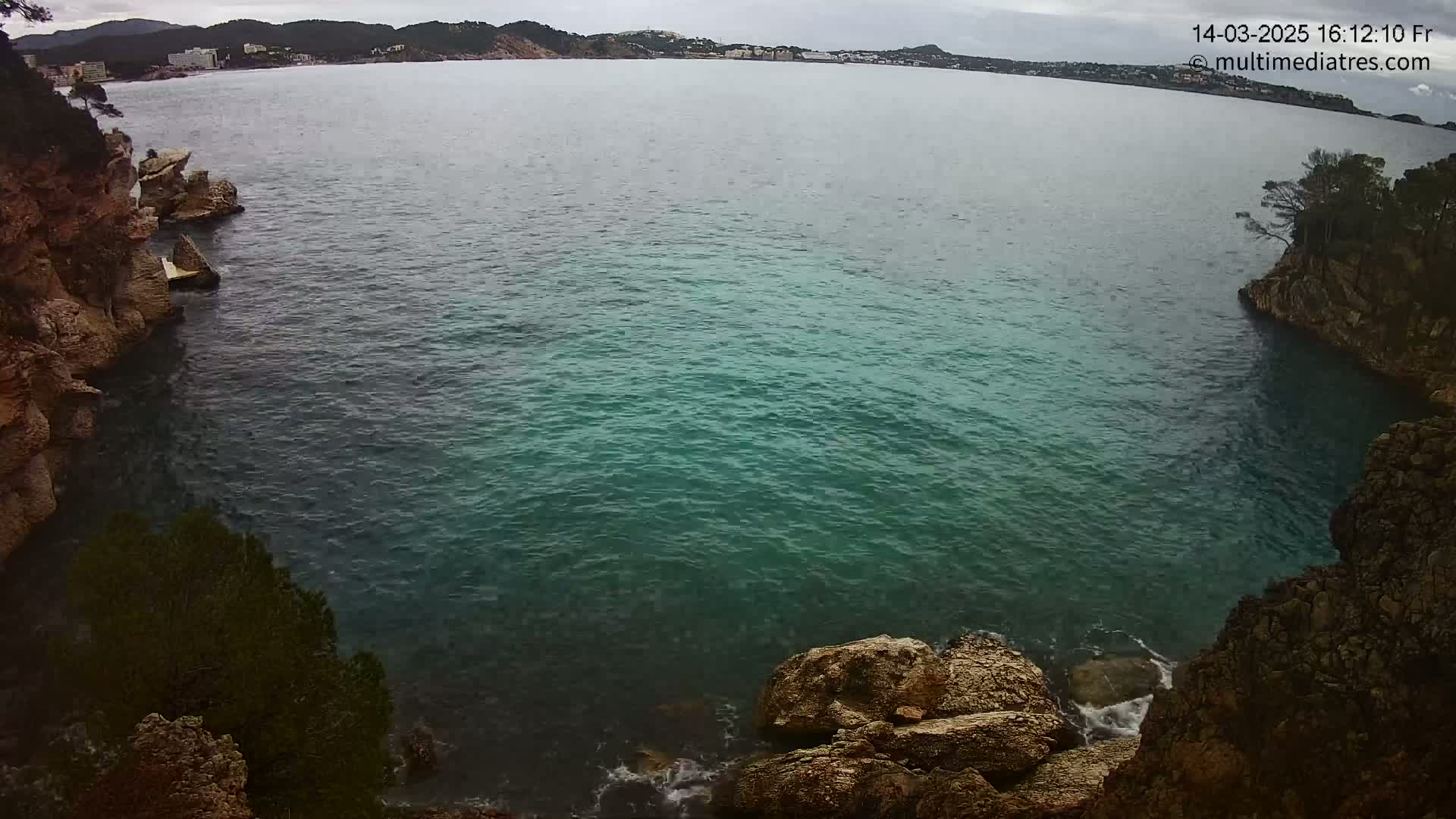 A cove of teal water is nestled between rocky cliffs on an overcast day.