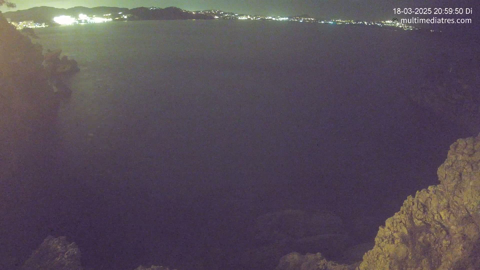 A nighttime view of a dark body of water with a distant, illuminated city skyline under a clear sky.