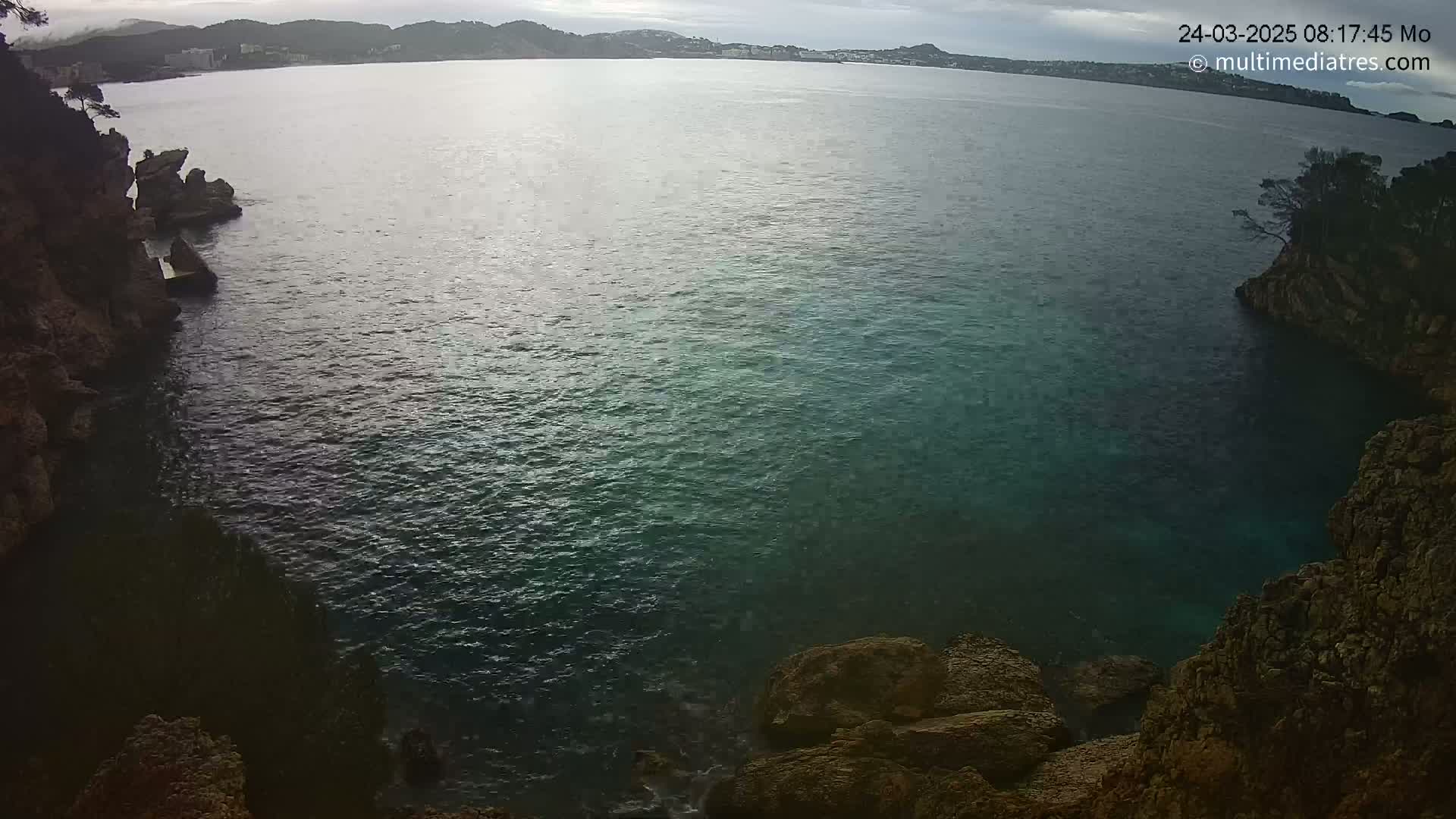 Dark, teal-colored water fills a cove bordered by dark, rocky cliffs under an overcast sky.