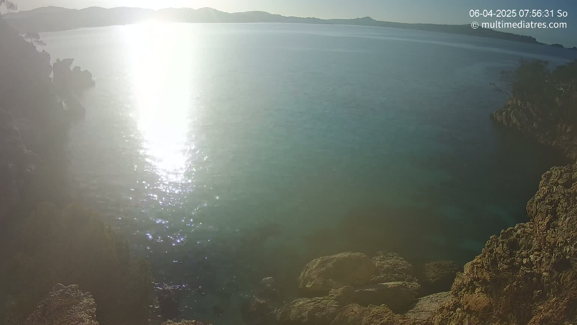 Rocky shores surround a calm, sunlit body of water under a clear sky.