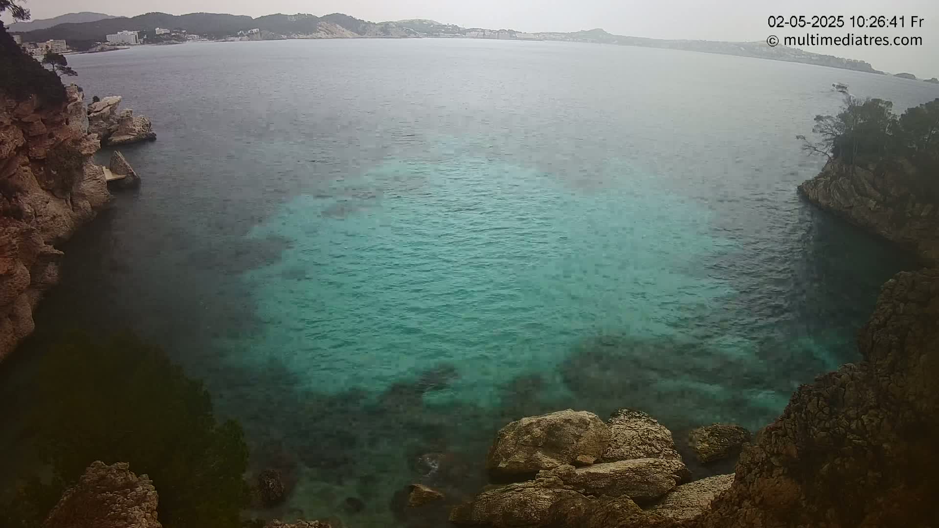 A cove of teal water is surrounded by rocky, tan cliffs under an overcast sky.
