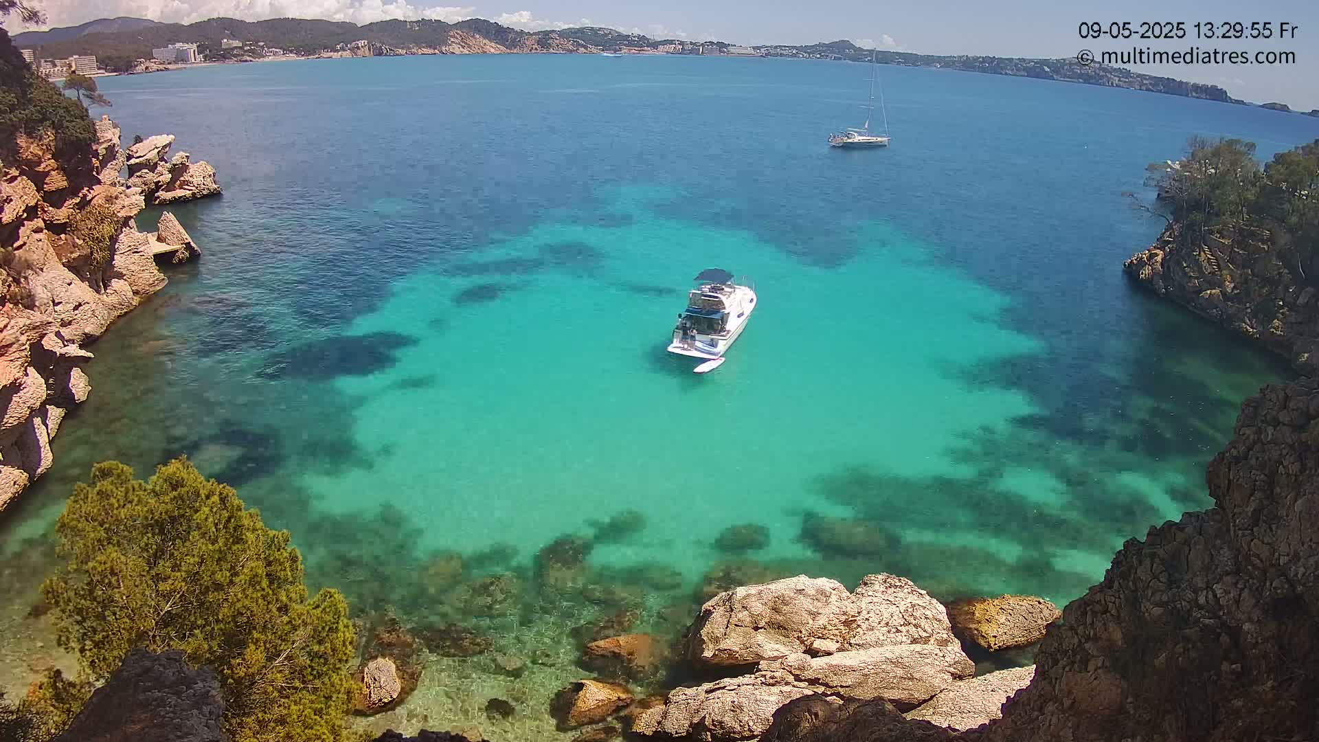 A motorboat is anchored in a clear, turquoise cove surrounded by rocky cliffs and vegetation under a sunny sky.