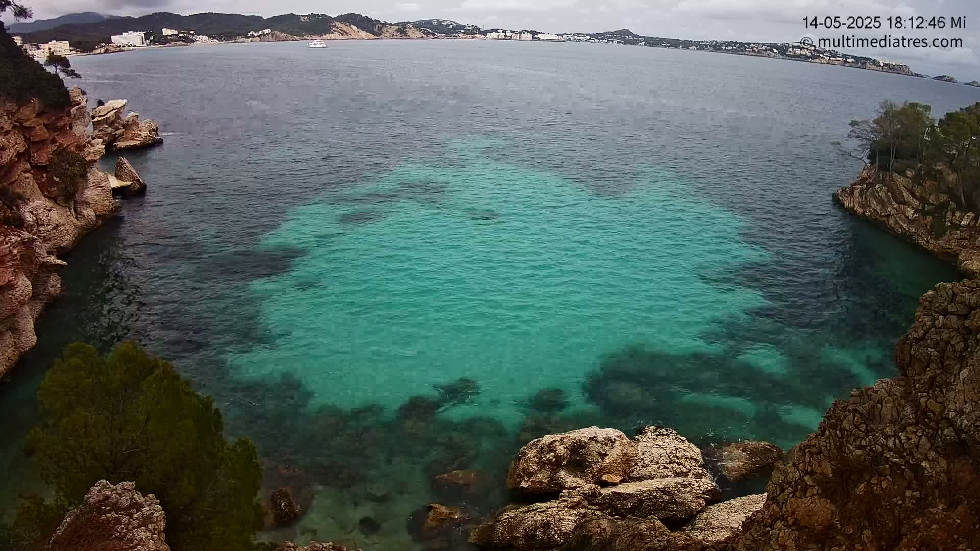 A cove of clear, teal water is nestled between rocky cliffs under an overcast sky.