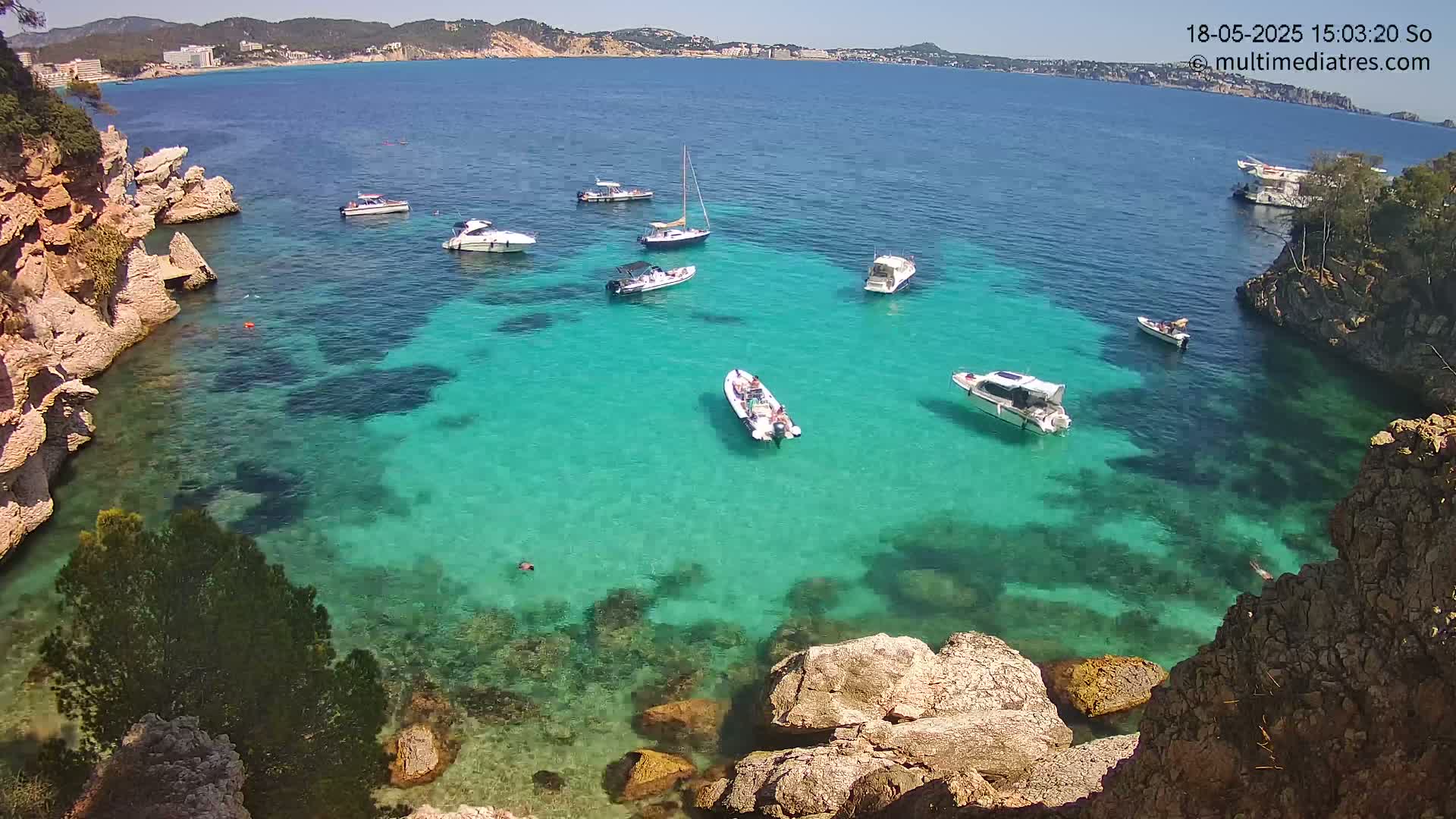 A cove with crystal-clear turquoise water is surrounded by rocky cliffs and several boats on a sunny day.