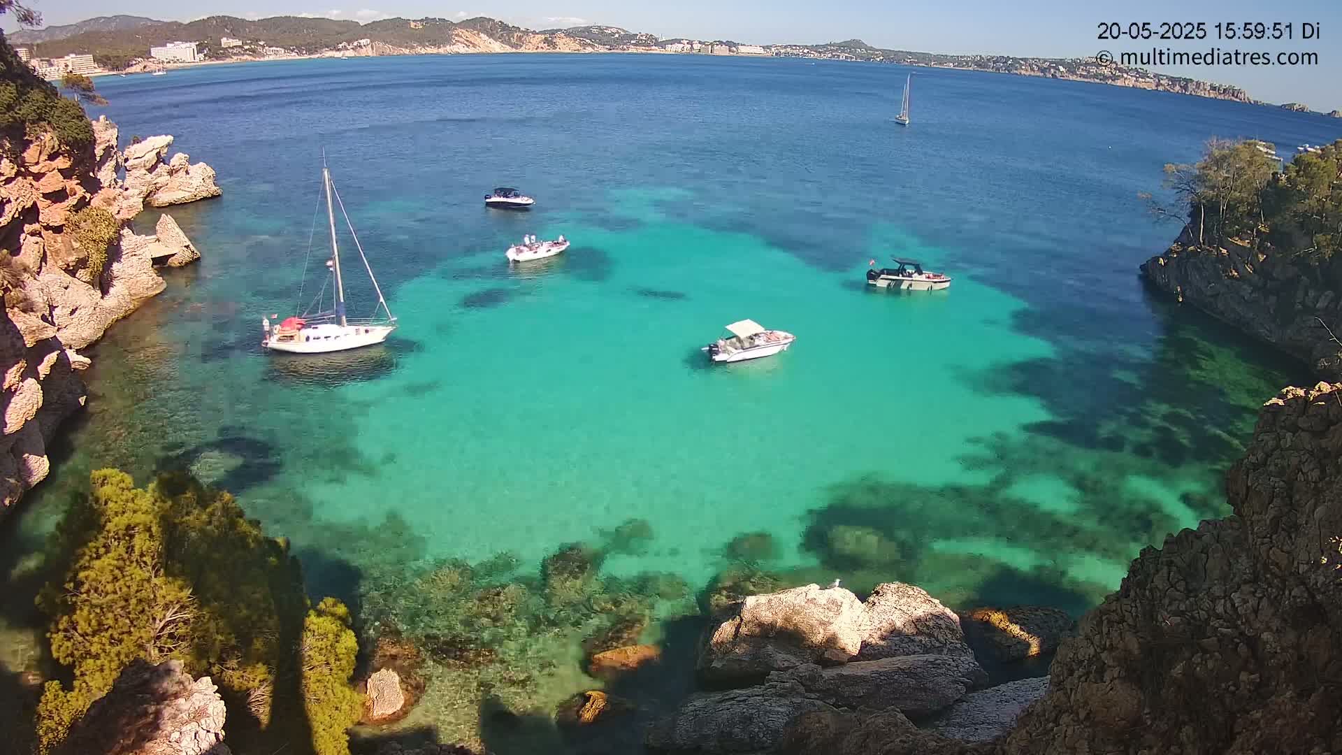 A tranquil cove with crystal-clear turquoise water, surrounded by rocky cliffs and several small boats, on a sunny day.