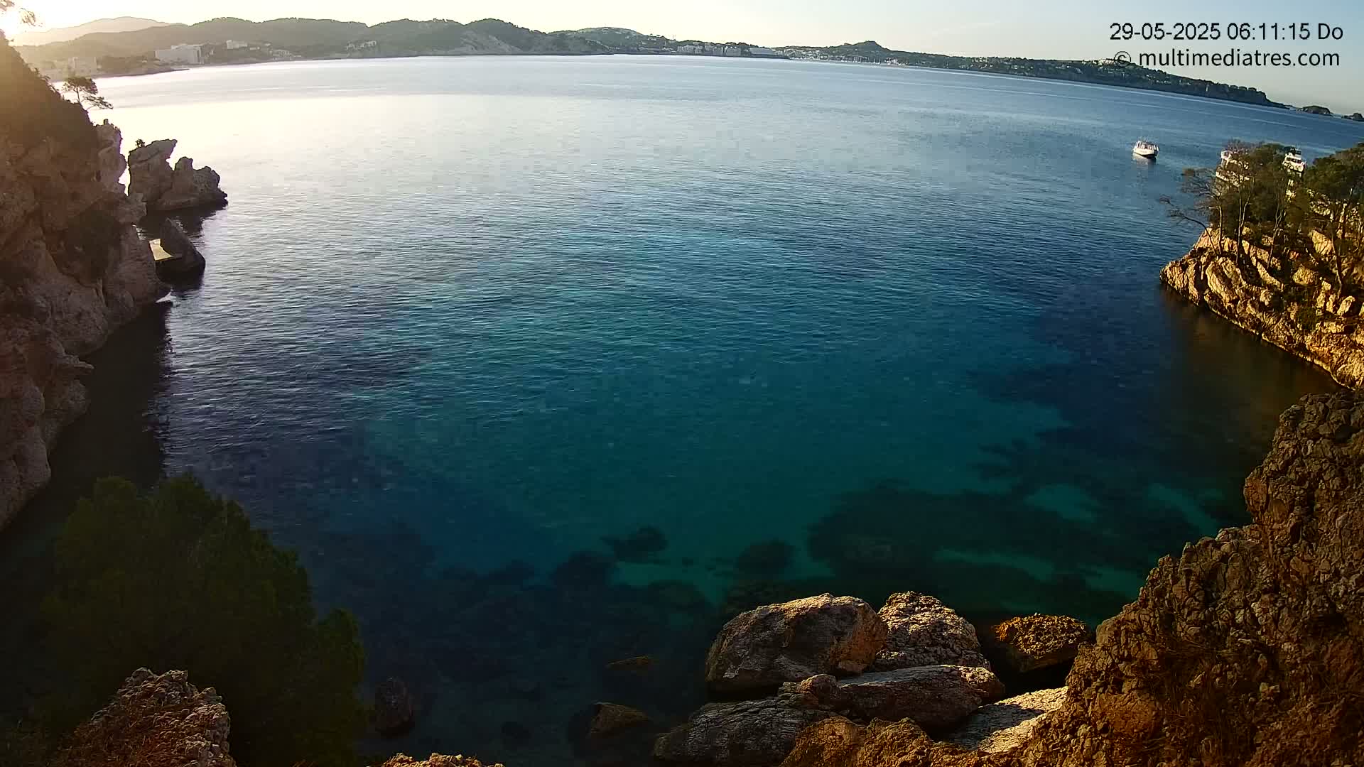 A calm, clear turquoise sea is nestled between rocky cliffs under a bright, sunny sky.