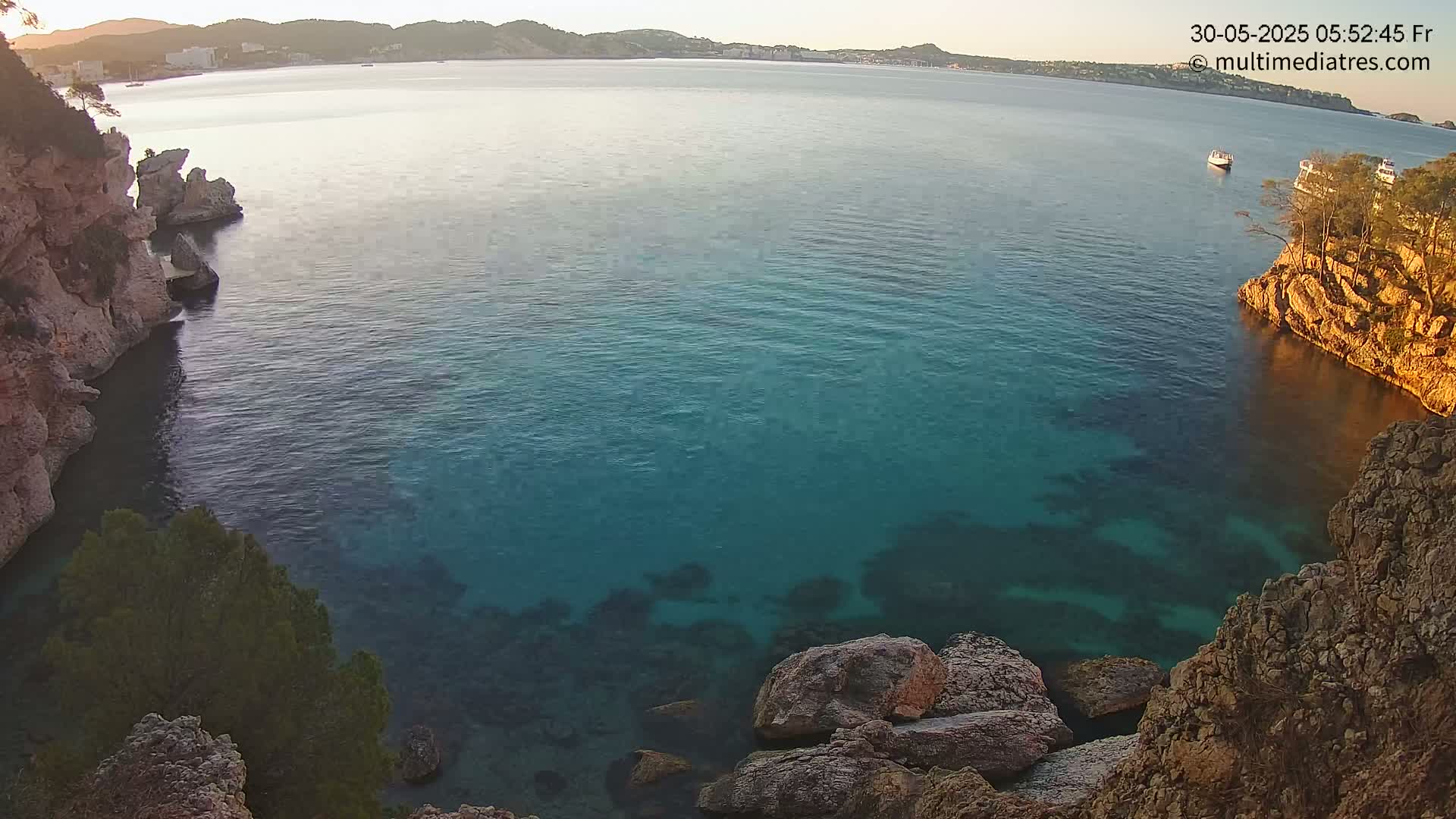 A calm, clear teal ocean cove is nestled between rocky cliffs under a sunrise sky.