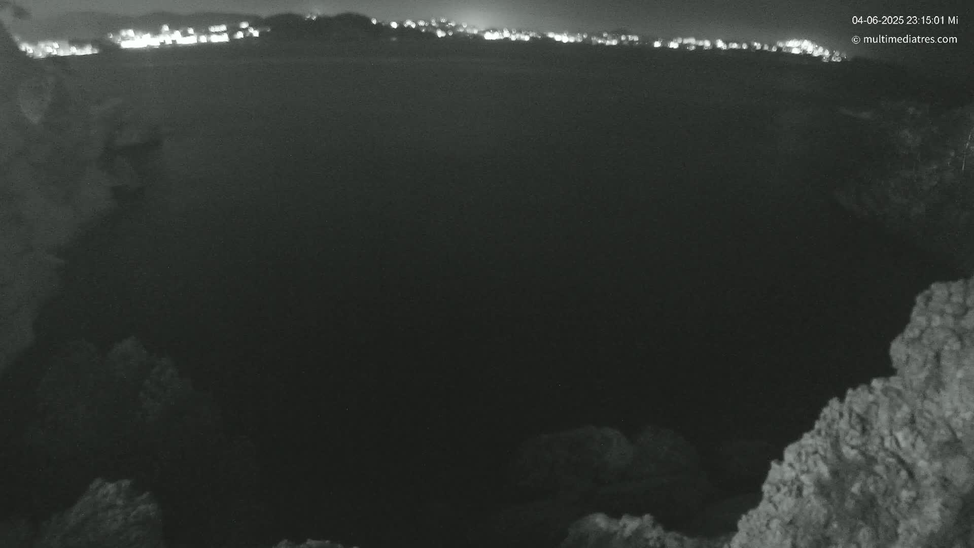 A nighttime, low-light view shows a dark body of water with a distant, illuminated shoreline.