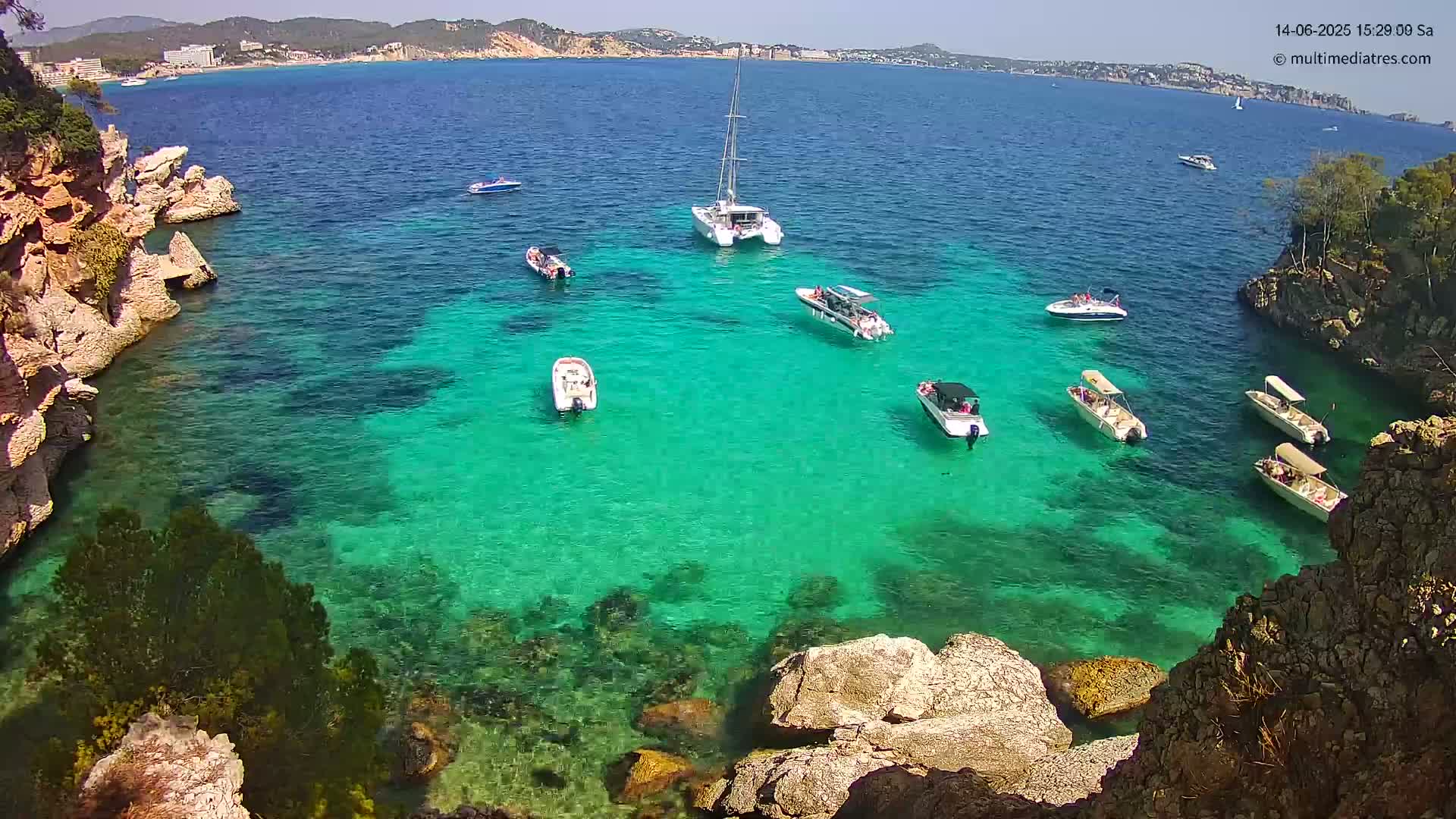 Brightly colored turquoise water filled with several boats is surrounded by rocky cliffs and land under a sunny sky.
