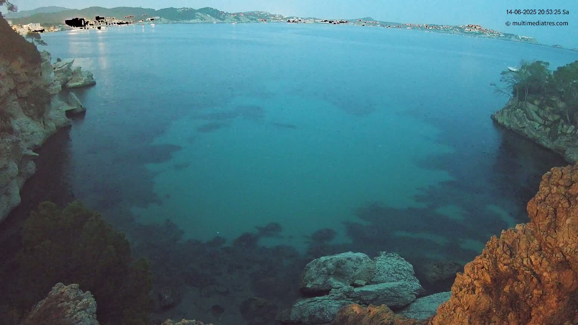 Brightly colored turquoise water filled with several boats is surrounded by rocky cliffs and land under a sunny sky.