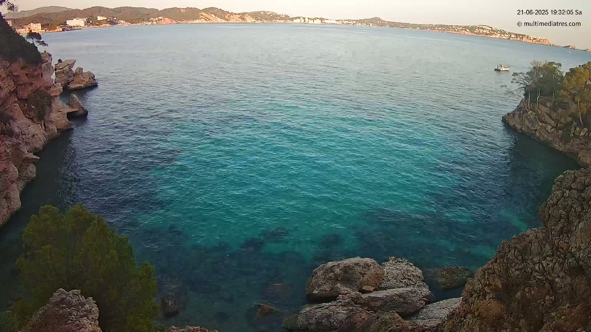 A calm, teal-colored sea is nestled between rocky shores, with a distant coastline visible under a clear sky.