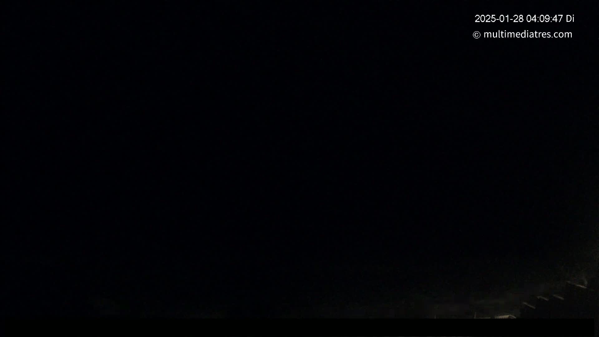 A nighttime, dark image shows a mostly black sky and the faint silhouettes of rooftops at the bottom.