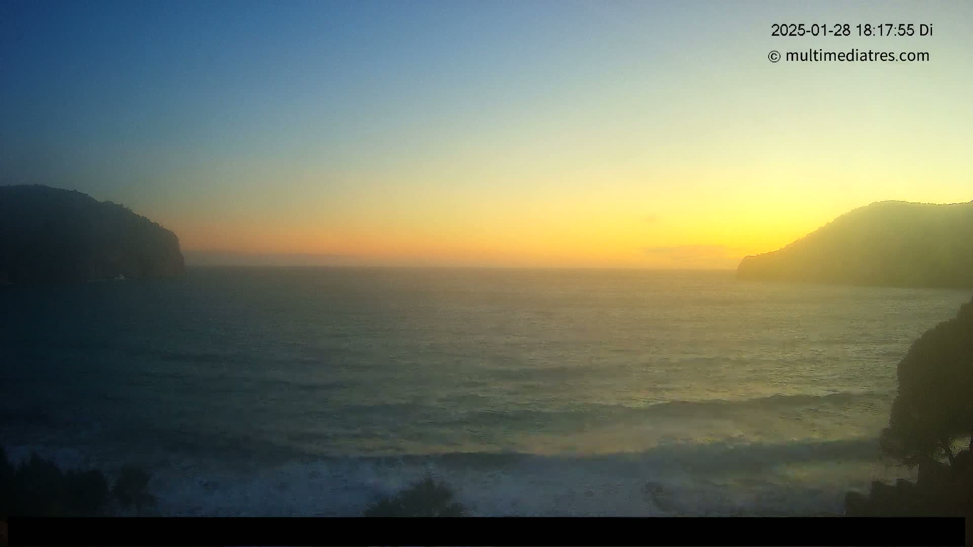 A hazy sunset over a wavy ocean, with dark hills on either side of the frame.