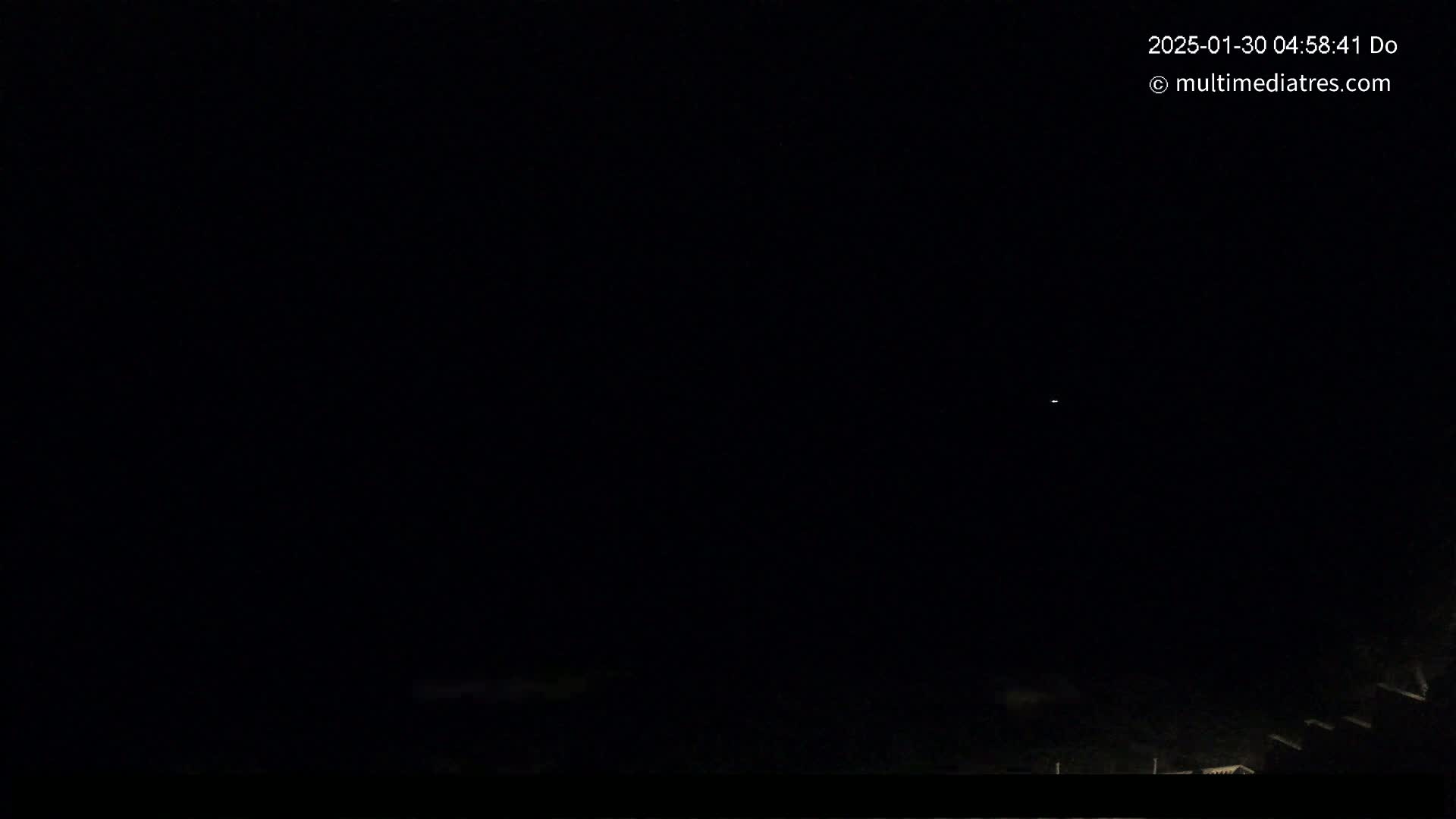A nighttime, dark scene shows a few faint lights in the distance at the bottom of the frame.